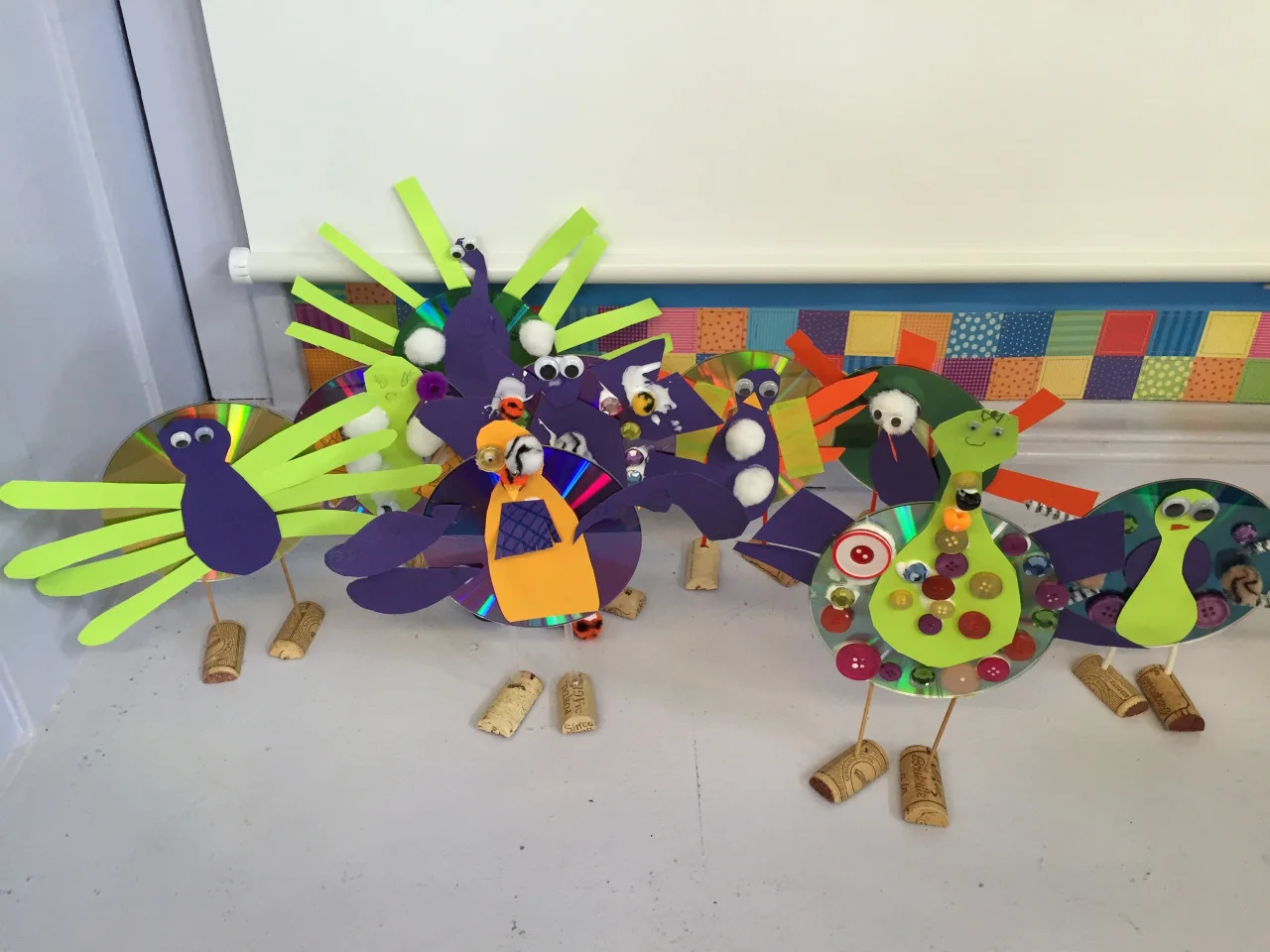 Class 1 Results: Peacocks? Turkeys? Insane hybrids? Ten girls and one boy who cried for the first 15 minutes of class. Adorable and rowdy and jacked up after consuming their pre-class snack of apple juice and Cheetos. (One girl asked, “Are Cheetos good for you?) Thank god I corralled a crafty friend to help because as soon as we were in the classroom it was excruciatingly clear that I had absolutely no control of the kids. My friend wrangled the group with a game while I set up the materials and plugged in the glue gun. I had thought this was a pretty straightforward creature to begin with. What I hoped would be easy – yeah, not so much. Just sticking the straws into the corks for the legs proved incomprehensible and impossible for tiny hands. “I don’t get it! Can you do it for me?” asked each and every kid. And forget making the plastic bag bodies. Paper would have to do, with help, of course, since even cutting was proving to be challenging. Paper and google eyes and corks were everywhere and I thought a fight was going to break out when one sweet girl found and commandeered all the fancy buttons and totally blinged out her peacock. Mental note: make sure to have enough shiny things for all. My friend and I took care of all of the gluing, and before we realized, it was time to clean up! With no help from the kids, natch! Live and learn!