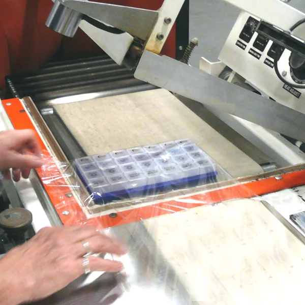close up of a person shrink wrapping a weekly pill container