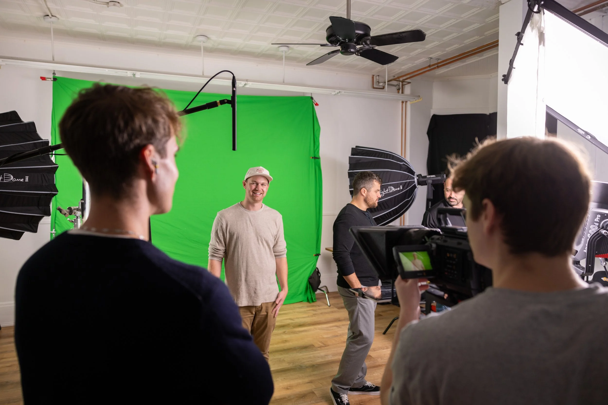 Group of people working on a video production with a green screen backdrop, professional lighting, and camera equipment in a studio.