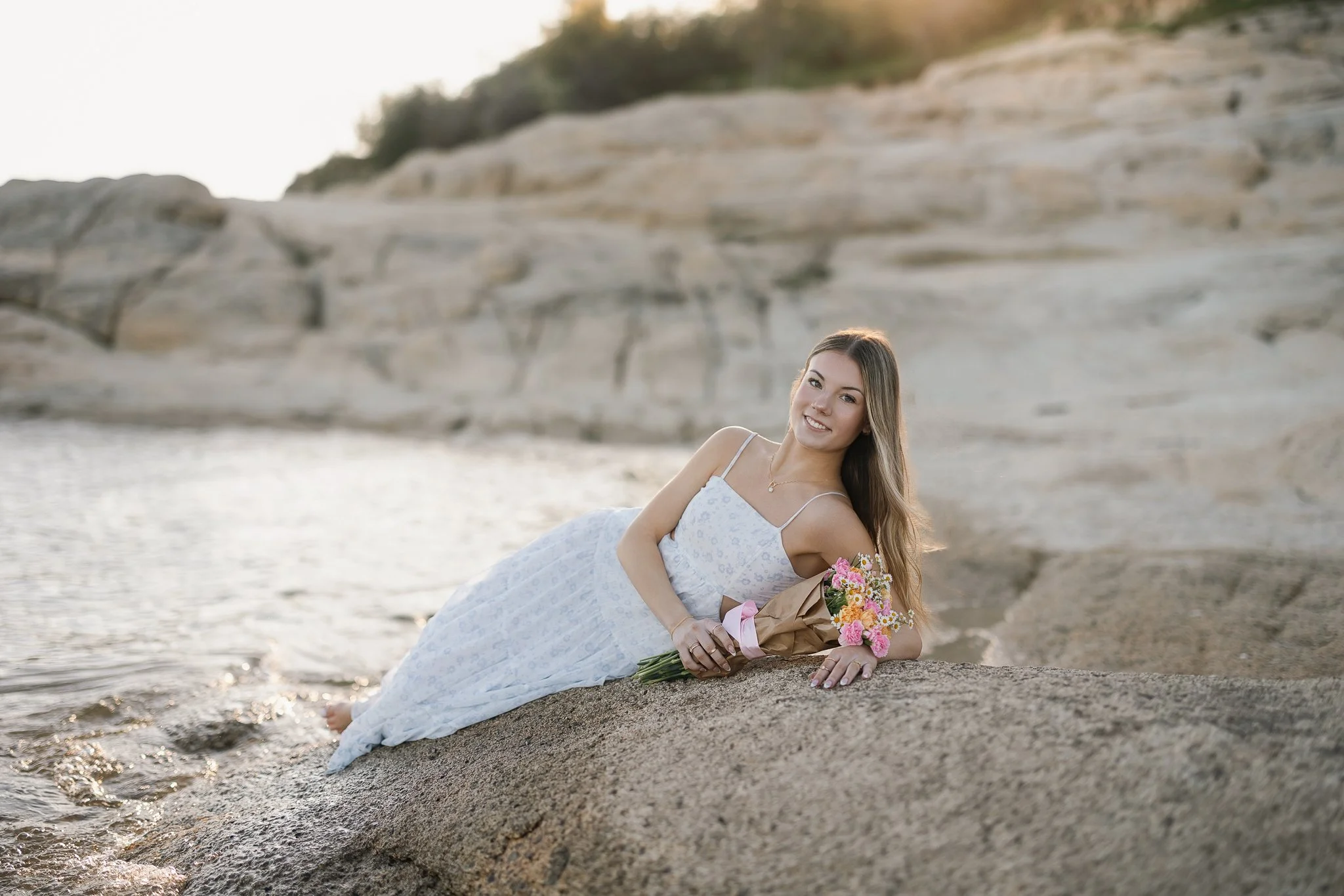 Folsom High School senior wearing a long flowy dress, holding flowers at Folsom lake for her senior pictures