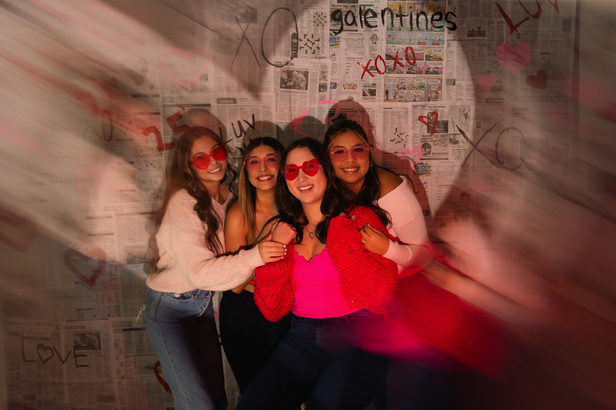 MC Senior VIP Team members wearing pink and red heart sunglasses during a fun Galentine’s Day group photoshoot with a Valentine-themed backdrop.