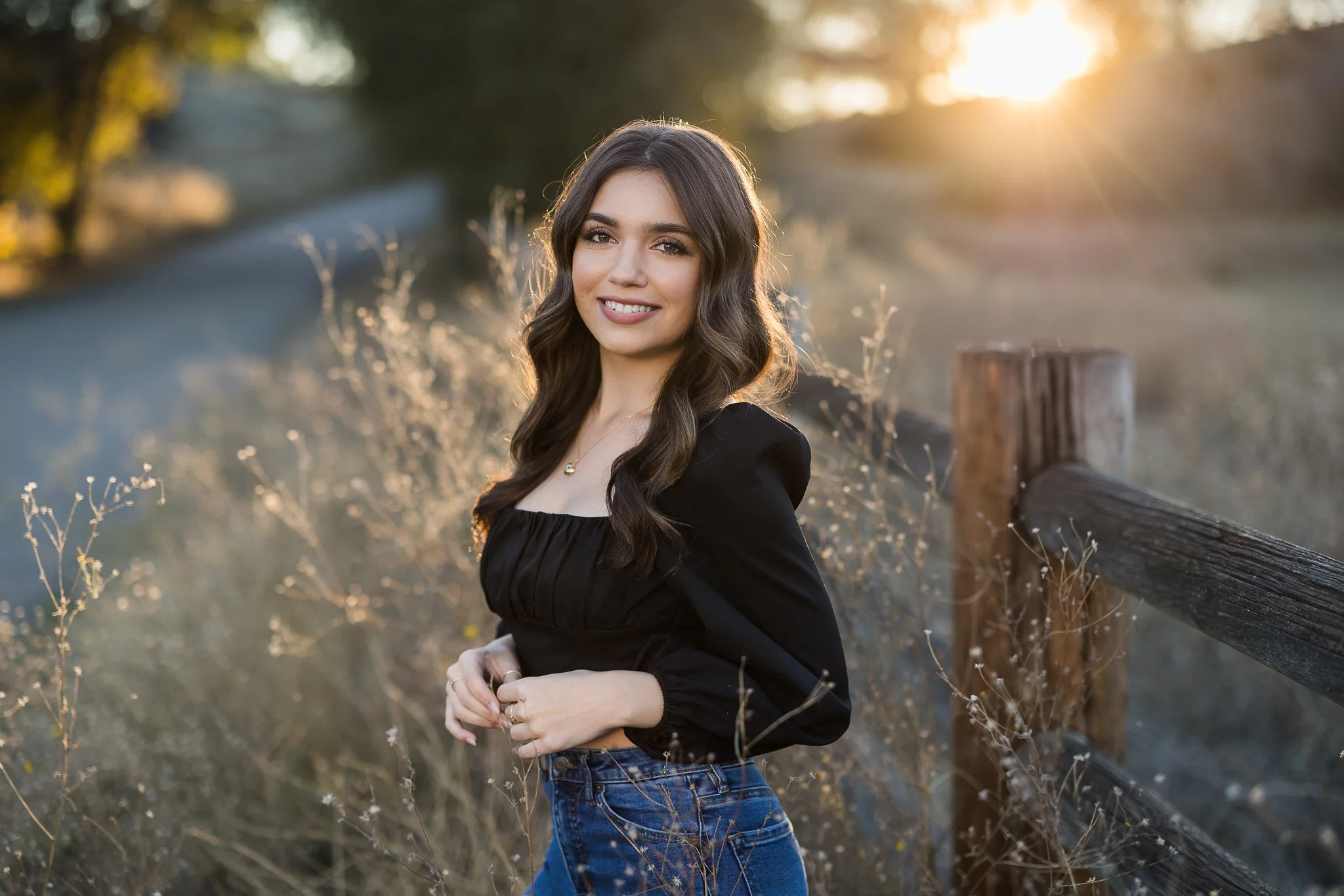Oakmont High School senior posing beside a rustic wood fence during golden hour, surrounded by tall grasses and warm fall light in Roseville, California.