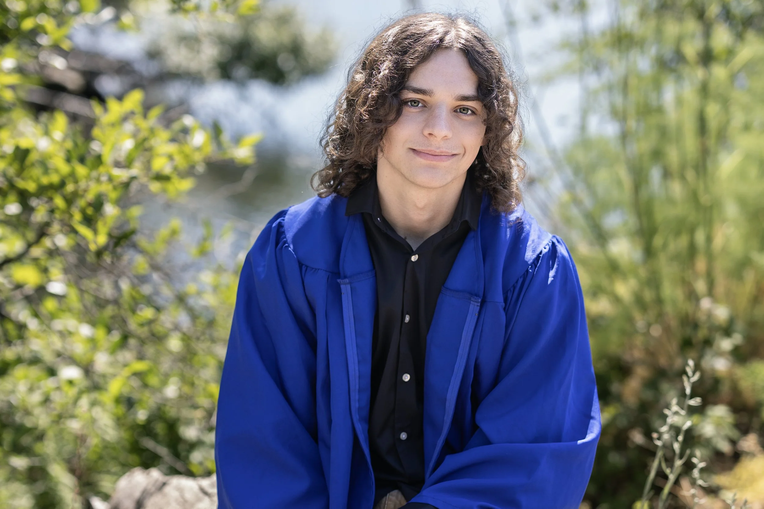 Senior picture idea for guys in a cap and gown featuring a Jesuit High School graduating senior in his blue graduation gown during an outdoor senior portrait session at Folsom Lake near Sacramento, California.
