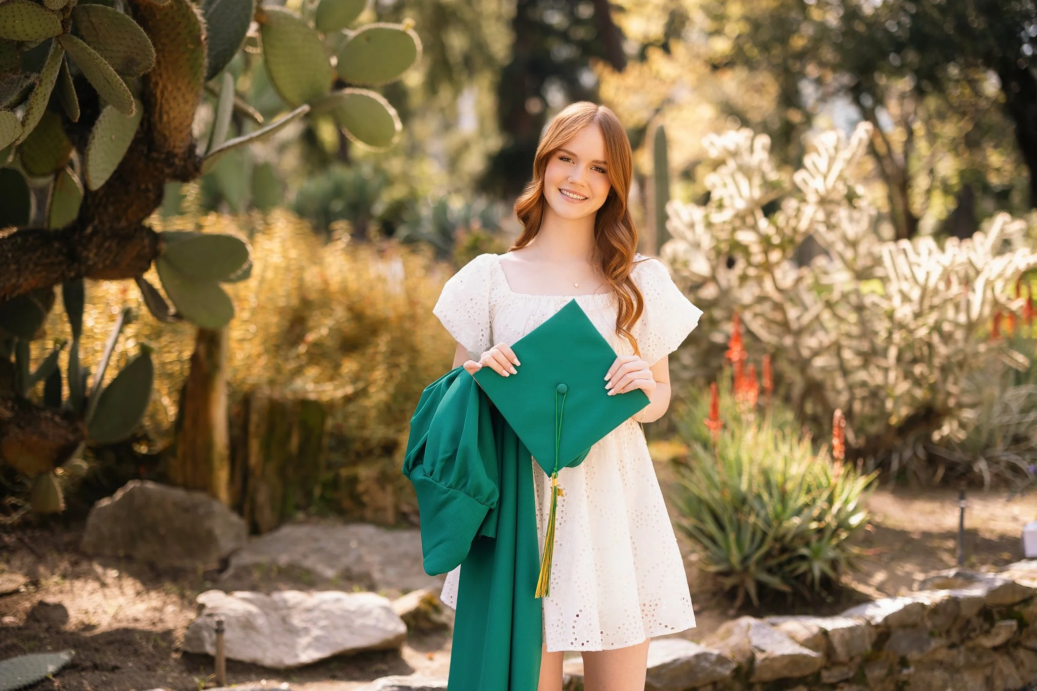 senior pictures of girl in a white dress with her cap n gown at the state capital garden