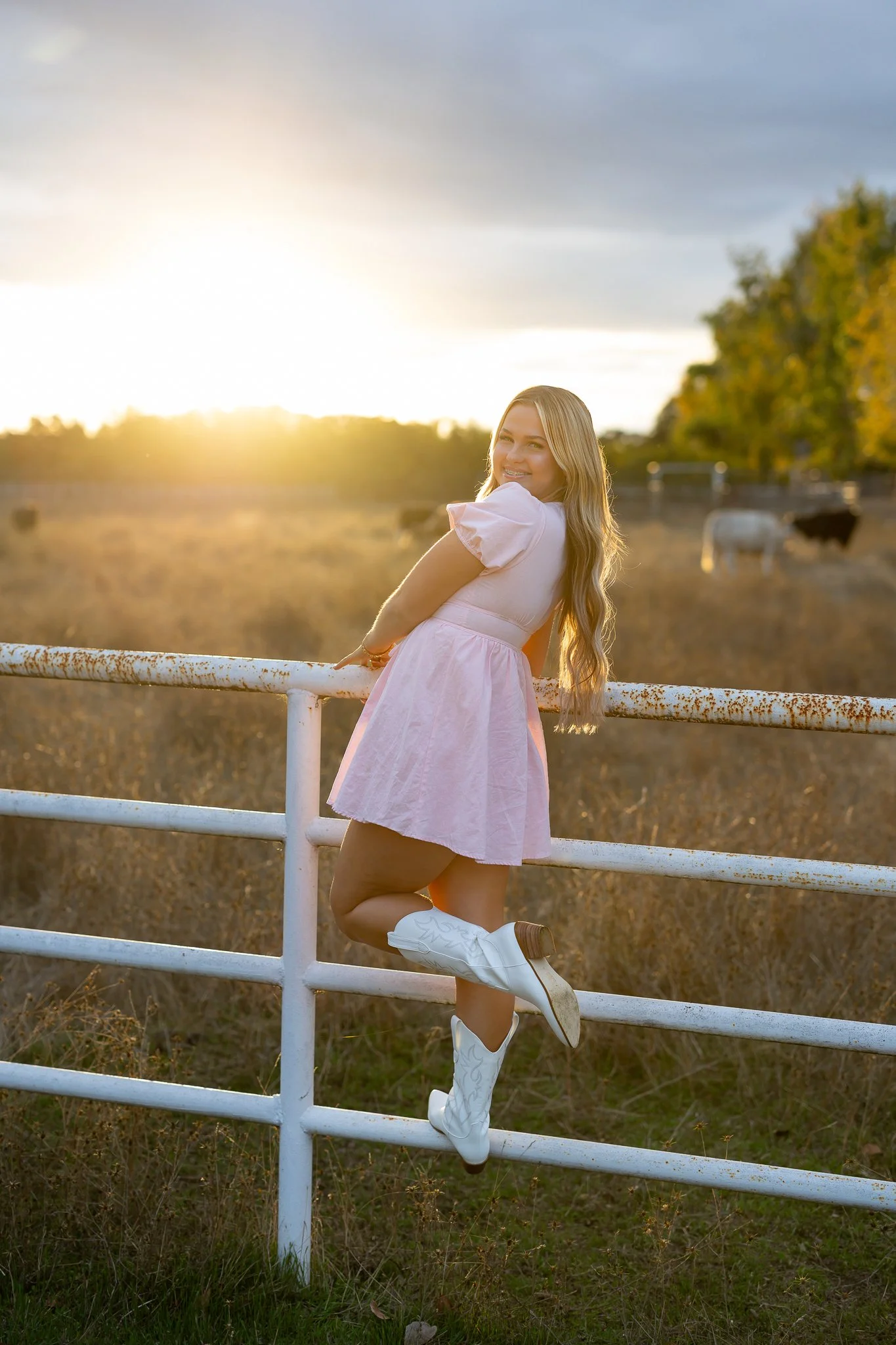 West Park High School senior girl in a pink dress and white cowboy boots posing on a ranch fence at golden hour in Roseville, California.