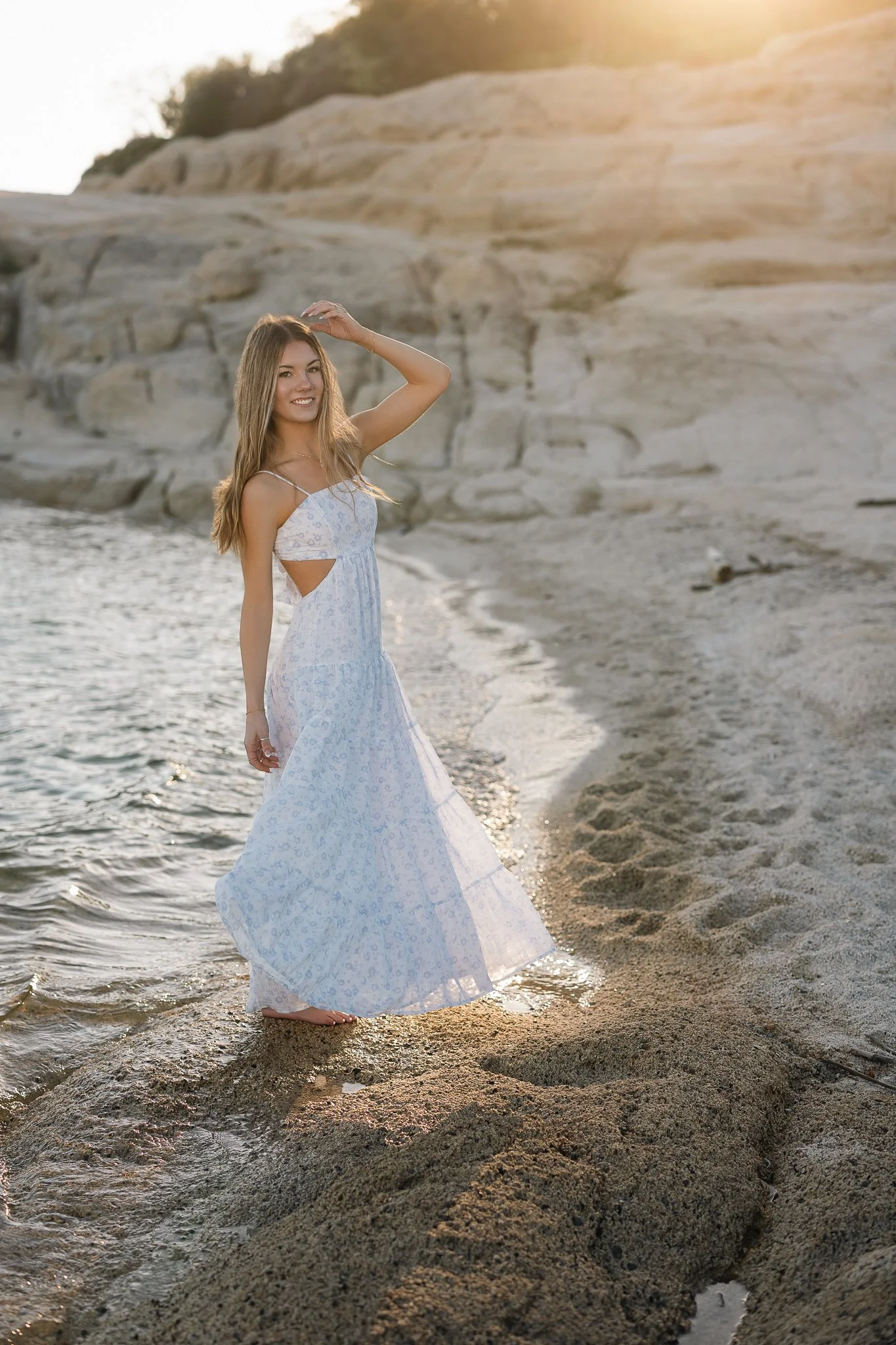 Granite Bay High School senior posing in a blue floral dress along the rocky shoreline at Folsom Lake during her senior pictures.