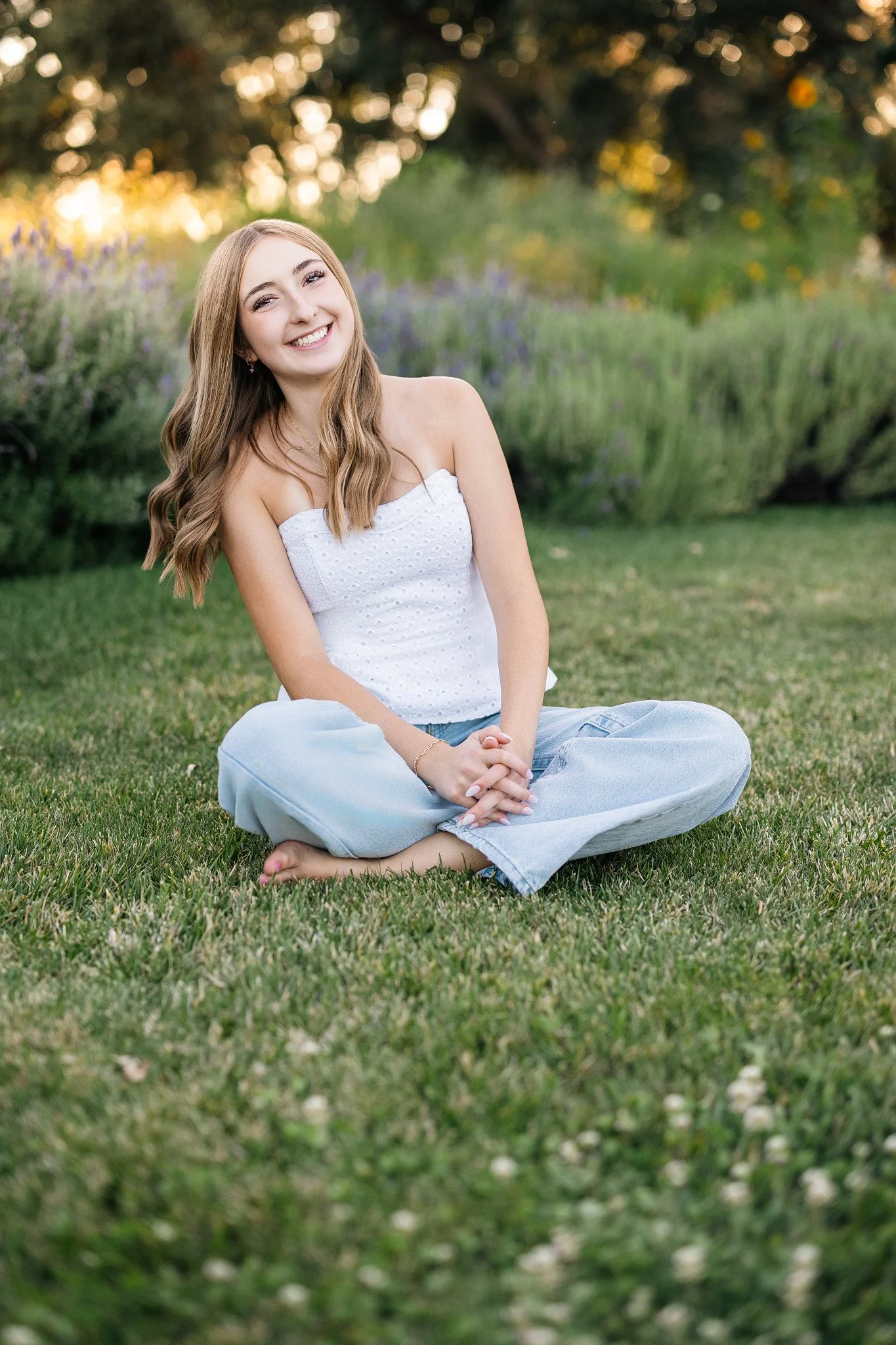 Lodi High School senior sitting in the grass surrounded by lavender and greenery during a golden hour senior picture session at Jessie’s Grove Winery in Lodi, California.