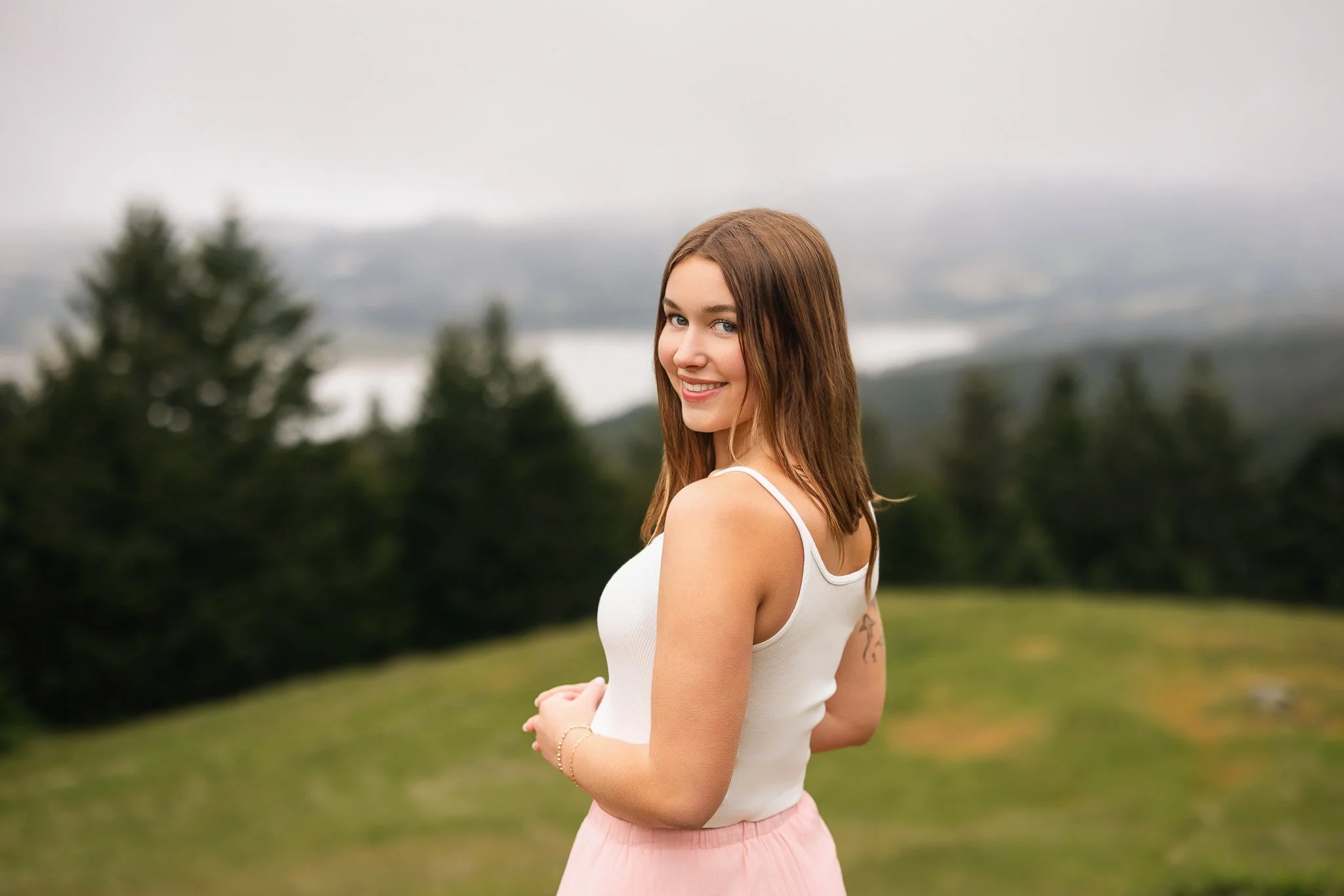Granite Bay High School senior smiling over her shoulder in a white tank top and pink skirt at Mount Tamalpais, with green hills and foggy scenery behind her.