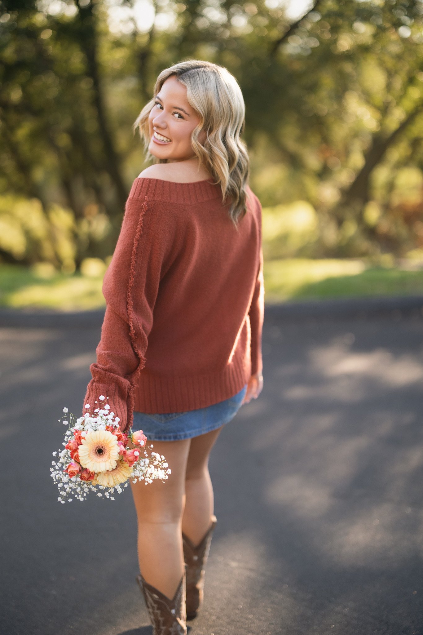 Fall senior pictures of a girl in a jean skirt and cowboy boots holding flowers