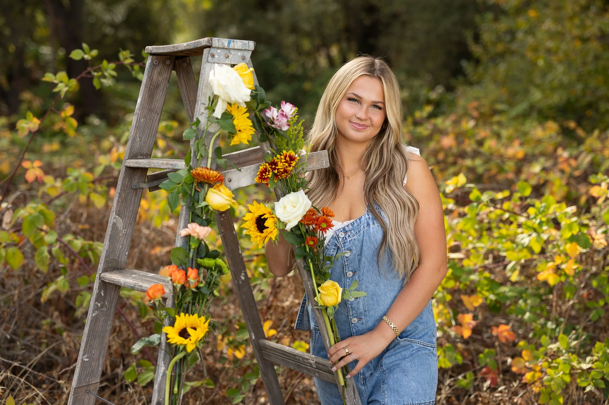 Roseville High School senior posing beside a rustic ladder decorated with colorful fall flowers during her outdoor senior portrait session in Roseville, California.