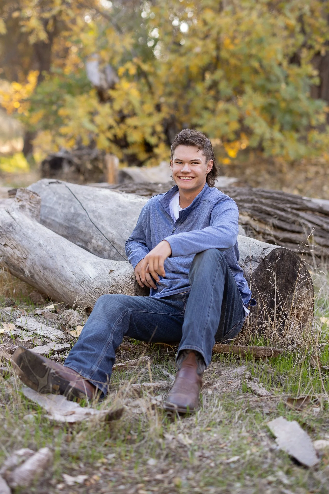 Cosumnes Oaks High School senior guy sitting beside a fallen log during fall senior pictures at the Cosumnes River Preserve near Elk Grove, California.