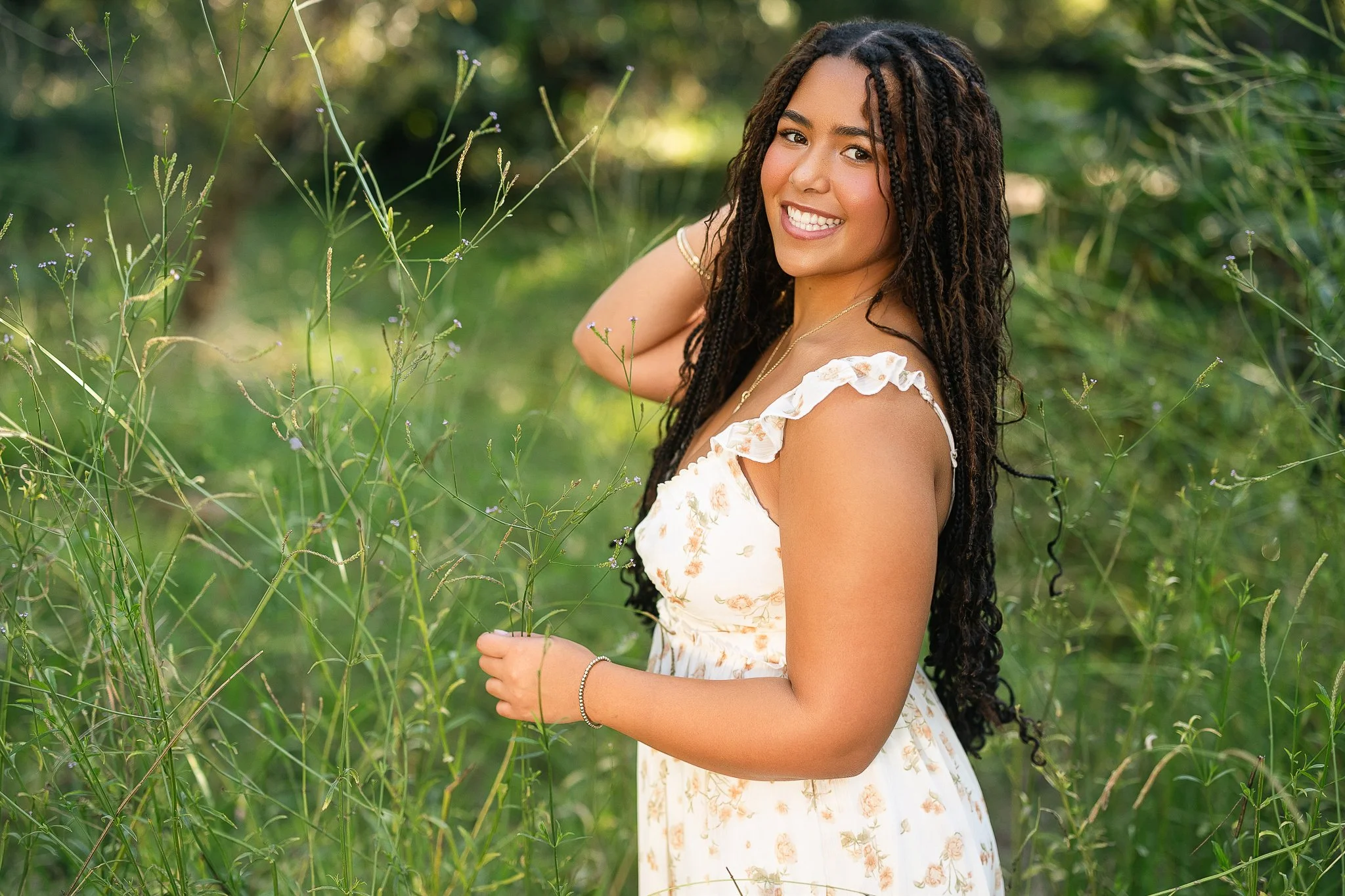 El Dorado Hills senior in a cream floral dress standing among tall wildflower grasses at golden hour during her fall senior session at Folsom Lake.