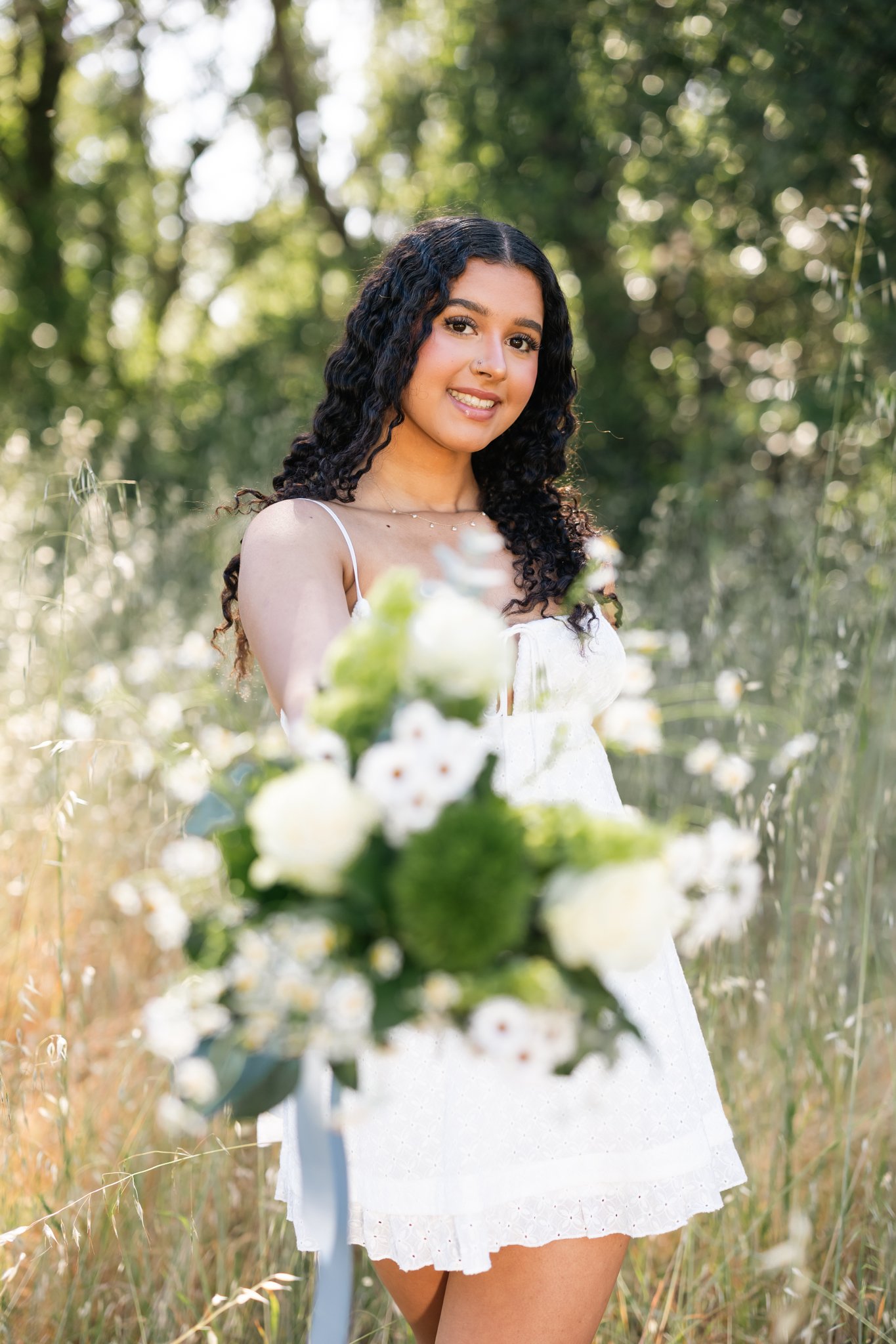 Senior pictures of a girl wearing a white dress in a field holding flowers