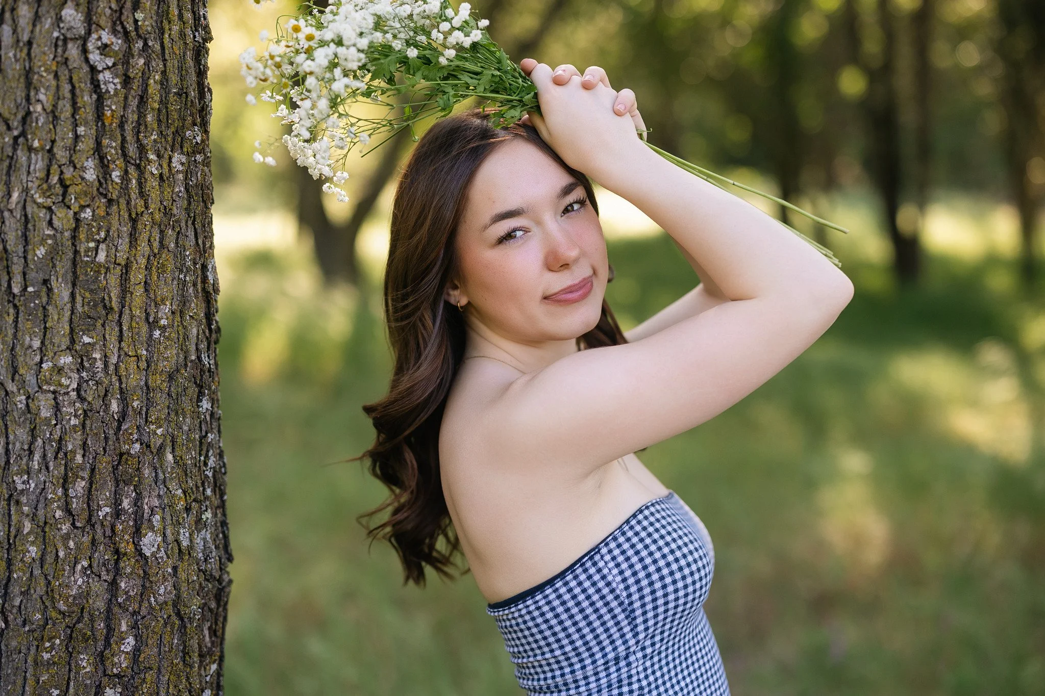 High school senior girl holding a bouquet of white flowers beside a tree during a spring senior portrait session at Maidu Regional Park in Roseville, California.