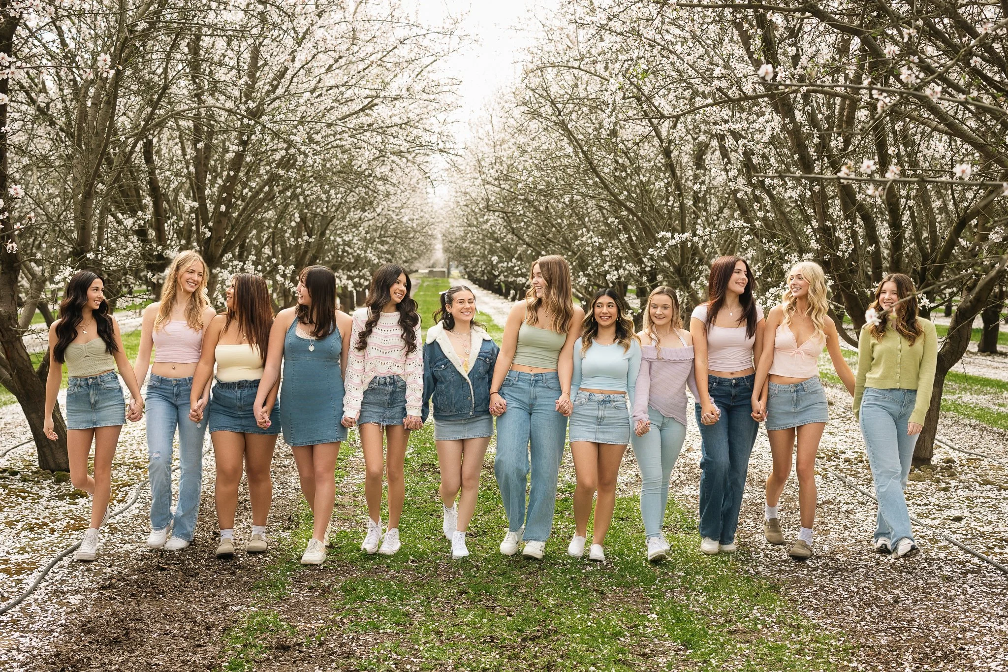 MC Senior VIP Team members walking together through blooming almond orchards during a spring senior team photoshoot in Northern California.
