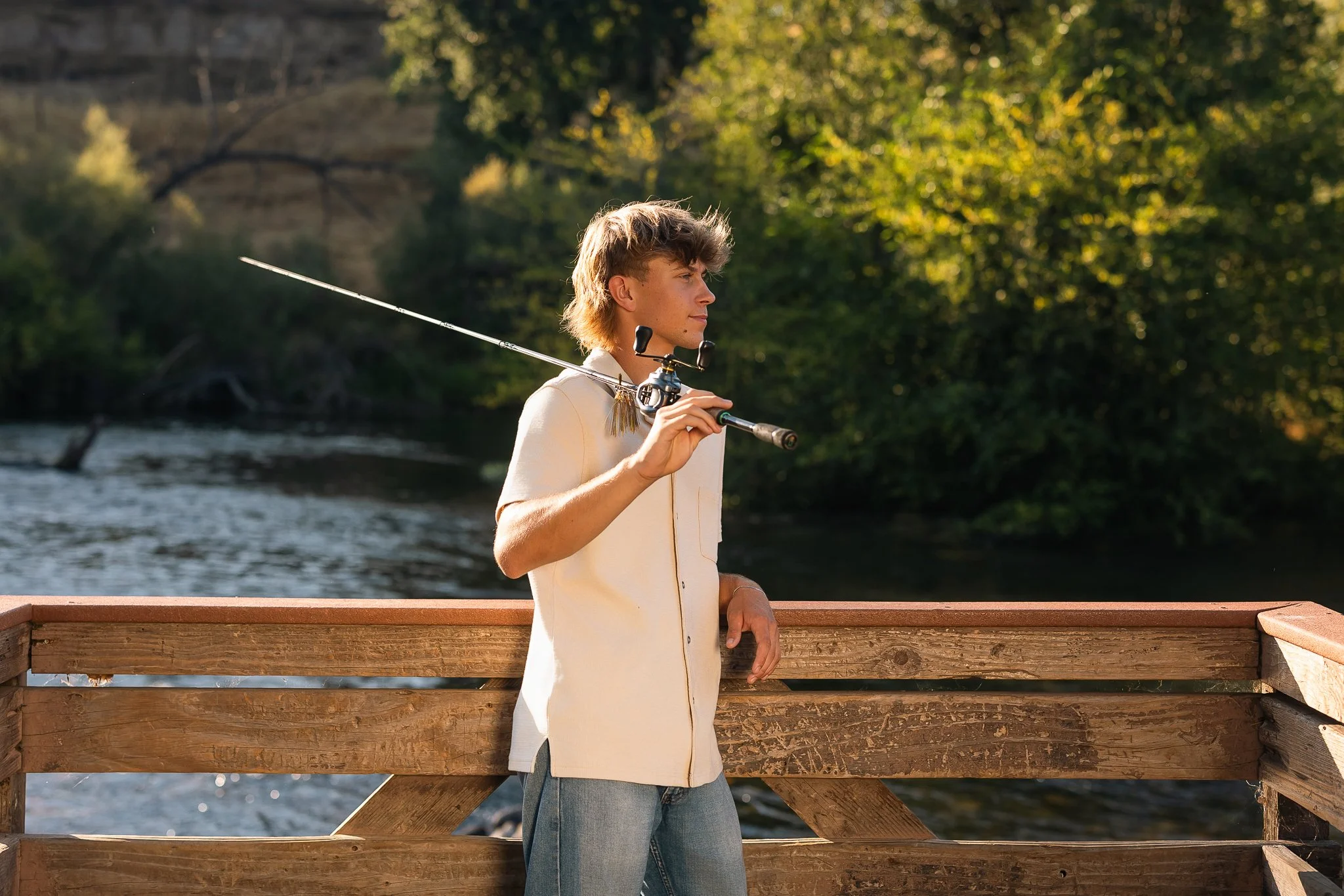Outdoor senior picture idea for guys featuring a Pleasant Grove High School senior with his fishing rod during a golden hour senior portrait session along the river near Sacramento, California.
