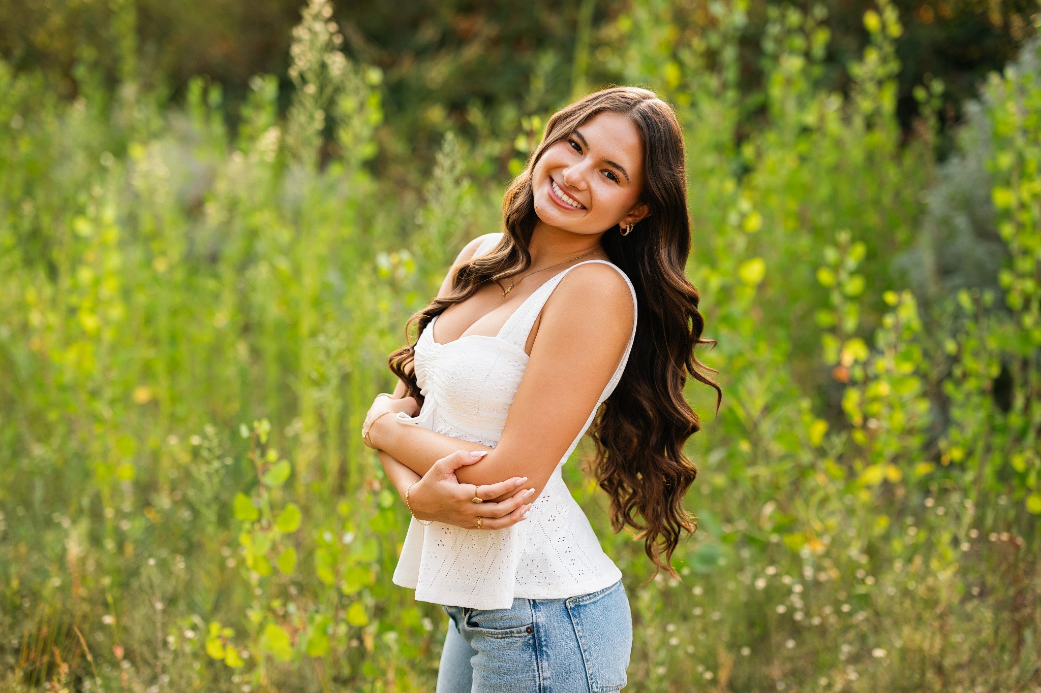 Lodi High School senior smiling in a white top and jeans surrounded by lush greenery during a golden hour senior portrait session near the Mokelumne River in Lodi, California.
