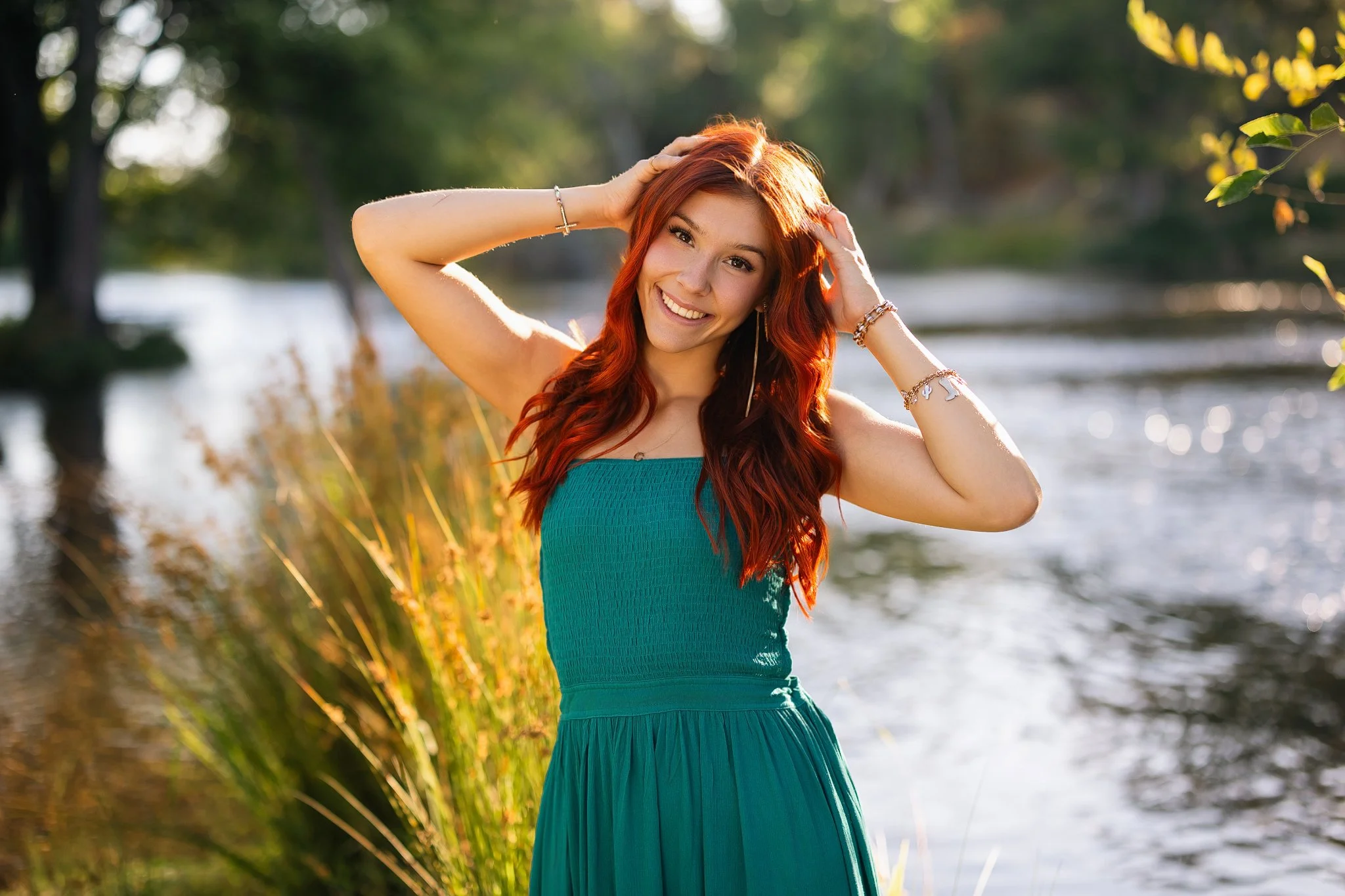 senior pictures of a girl with red hair in a green dress by the water