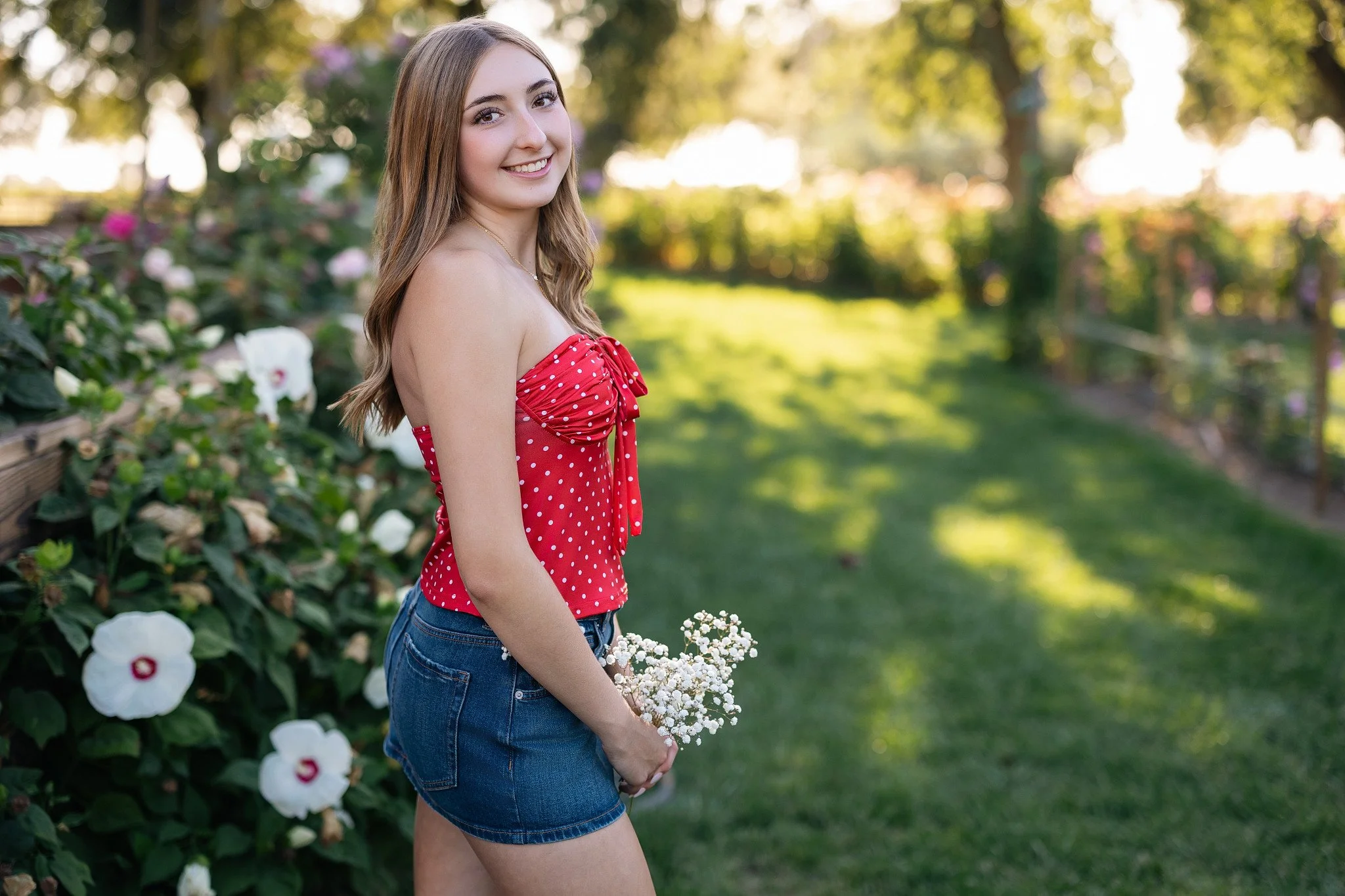 Lodi High School senior posing with a small bouquet during a summer senior picture session surrounded by flowers and greenery in Lodi, California.