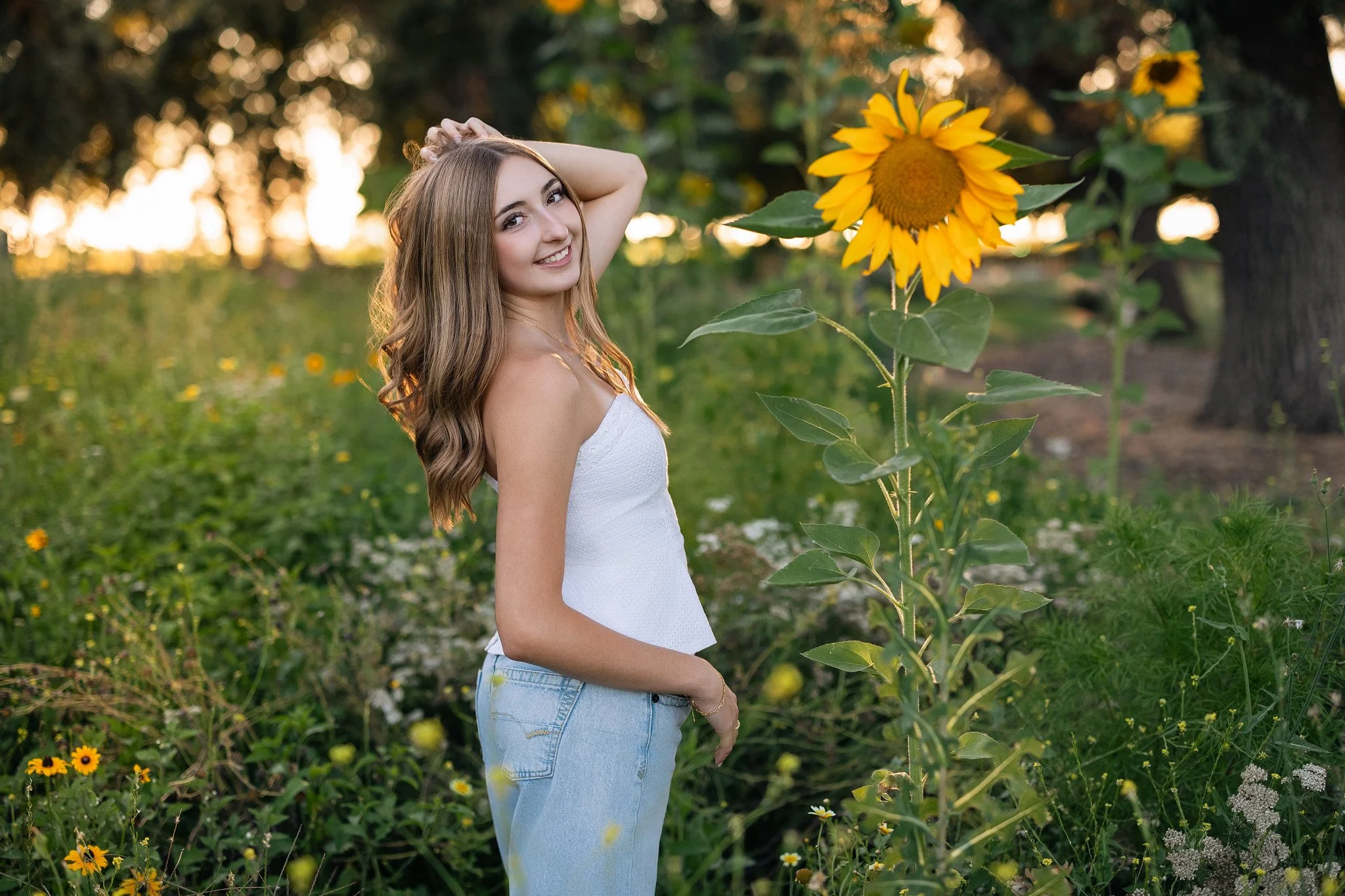 Lodi high school graduating senior posing beside a tall sunflower during golden hour at Oak Grove Flower Farm at Jessie’s Grove Winery in Lodi, California.