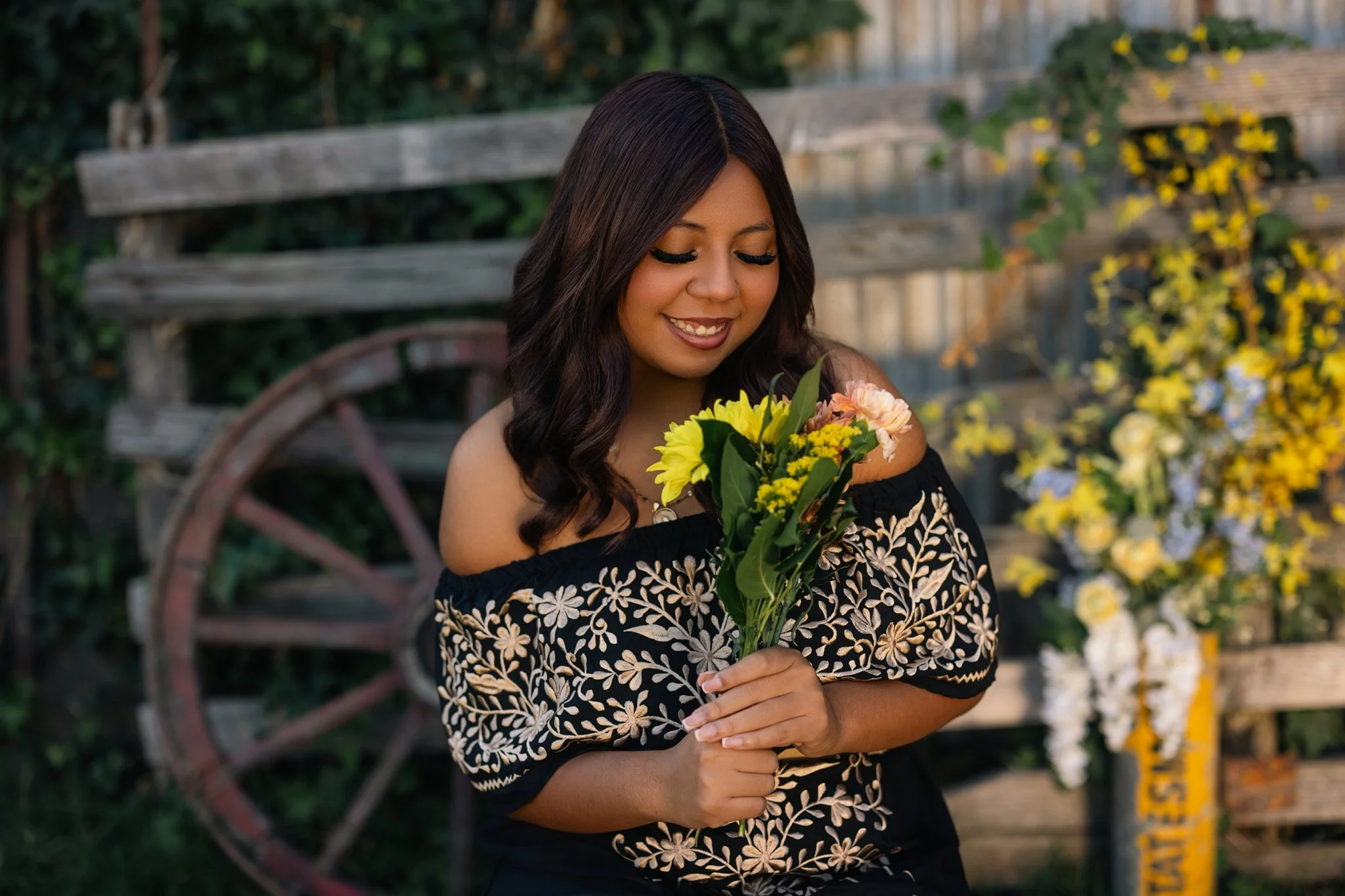 Linden High School senior holding a colorful bouquet during her senior portrait session at West 12 Ranch, with a rustic wood fence and wagon wheel in the background.