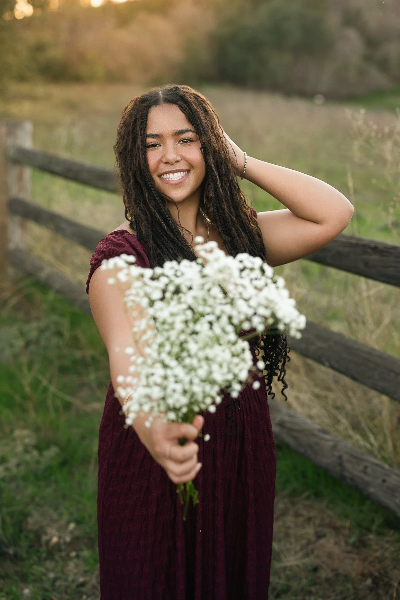 High school senior girl pictures holding flowers in a field with a fence in a long flowy dress in Folsom, Ca