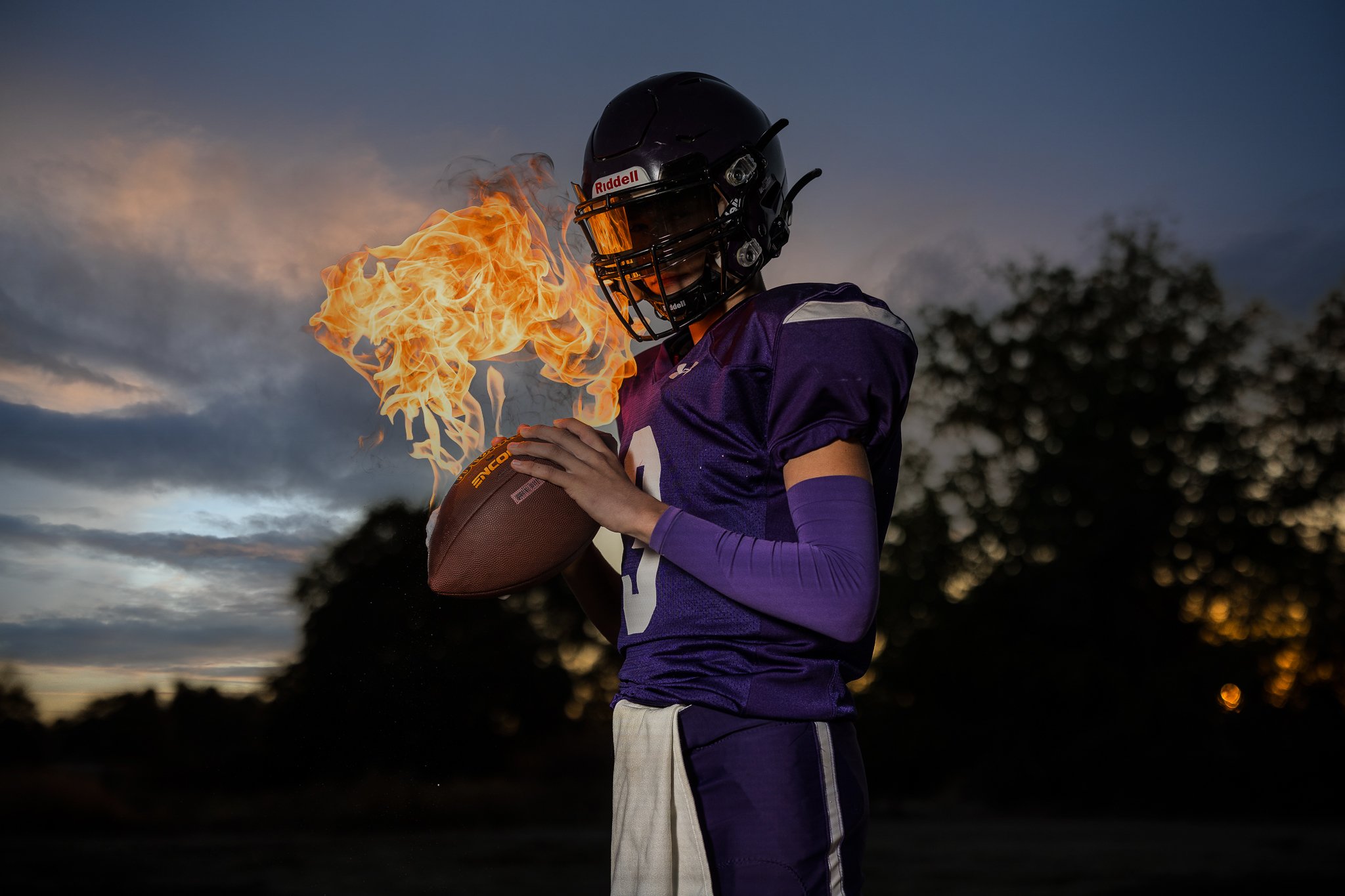Unique senior picture idea for guys featuring an Amador Valley High School football player in his uniform holding a football with flames at a private Northern California ranch.