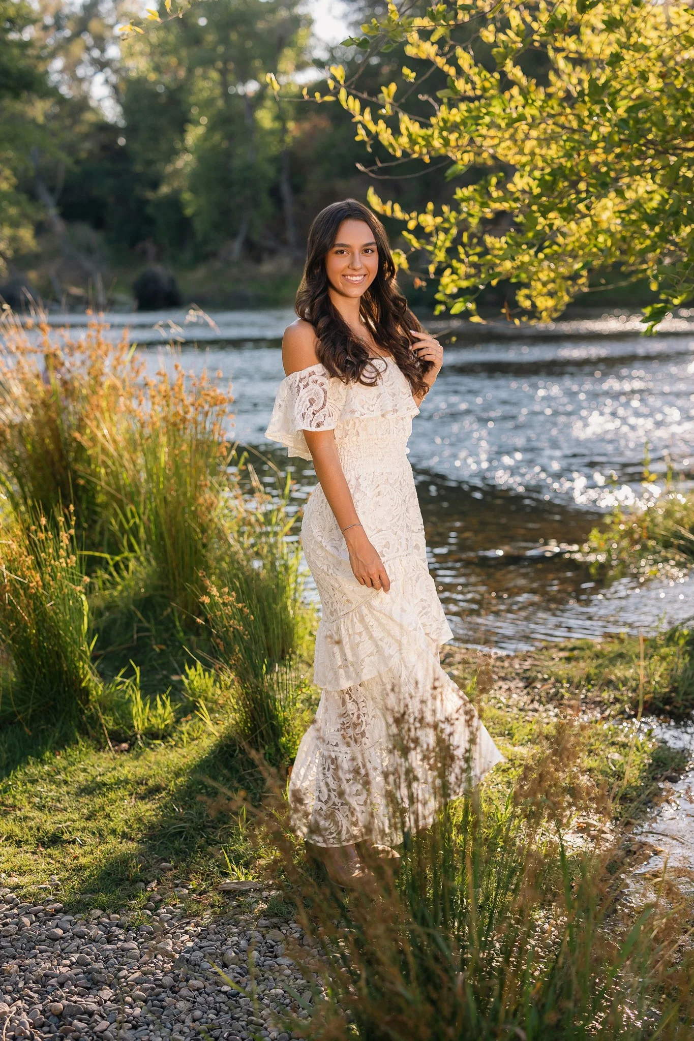 Pleasant Grove High School senior posing in a white lace dress beside the water during golden hour for her Elk Grove senior pictures.