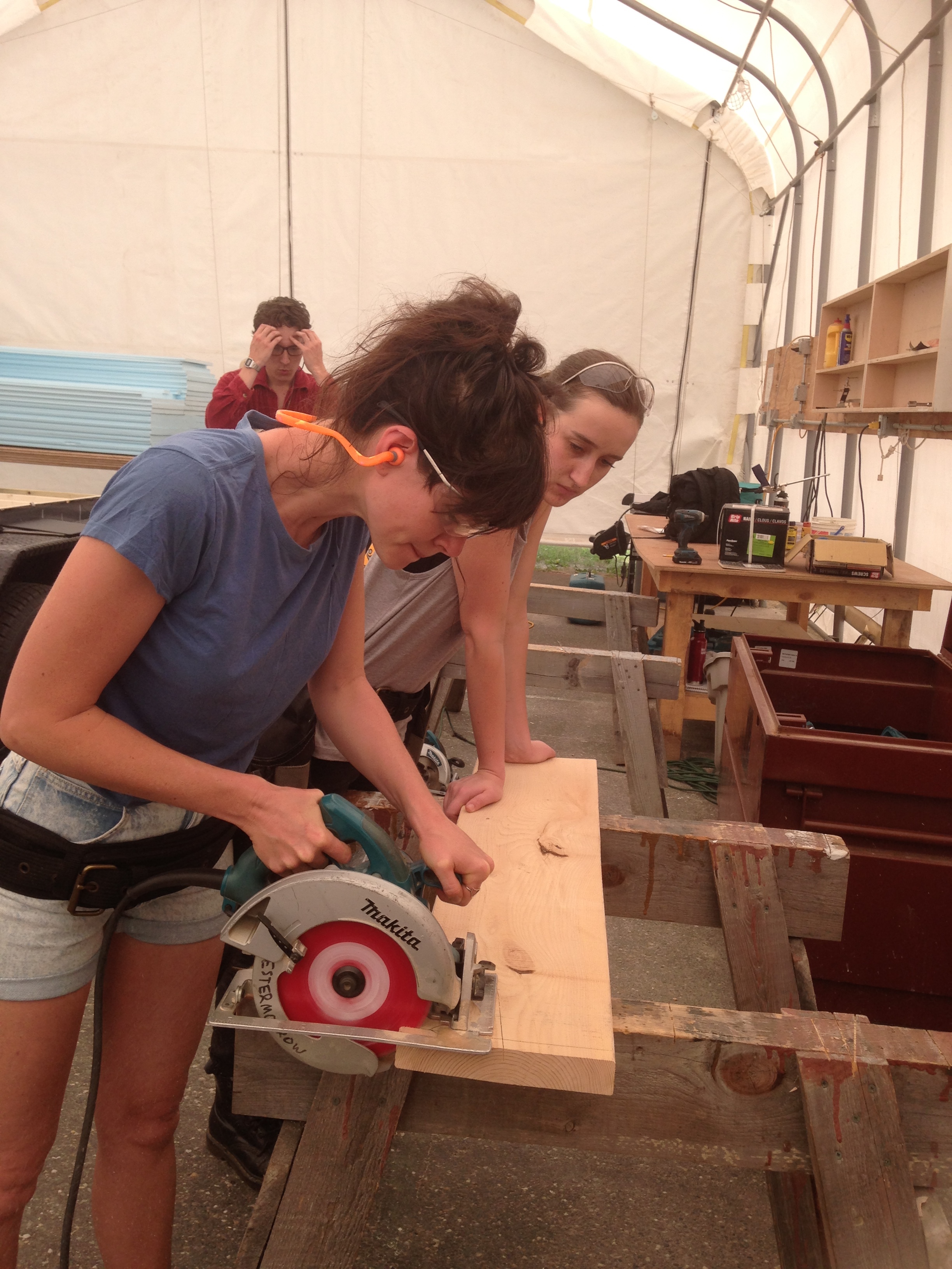 Lauren practices cutting with the circular saw while Tori looks on (and holds the board steady!)