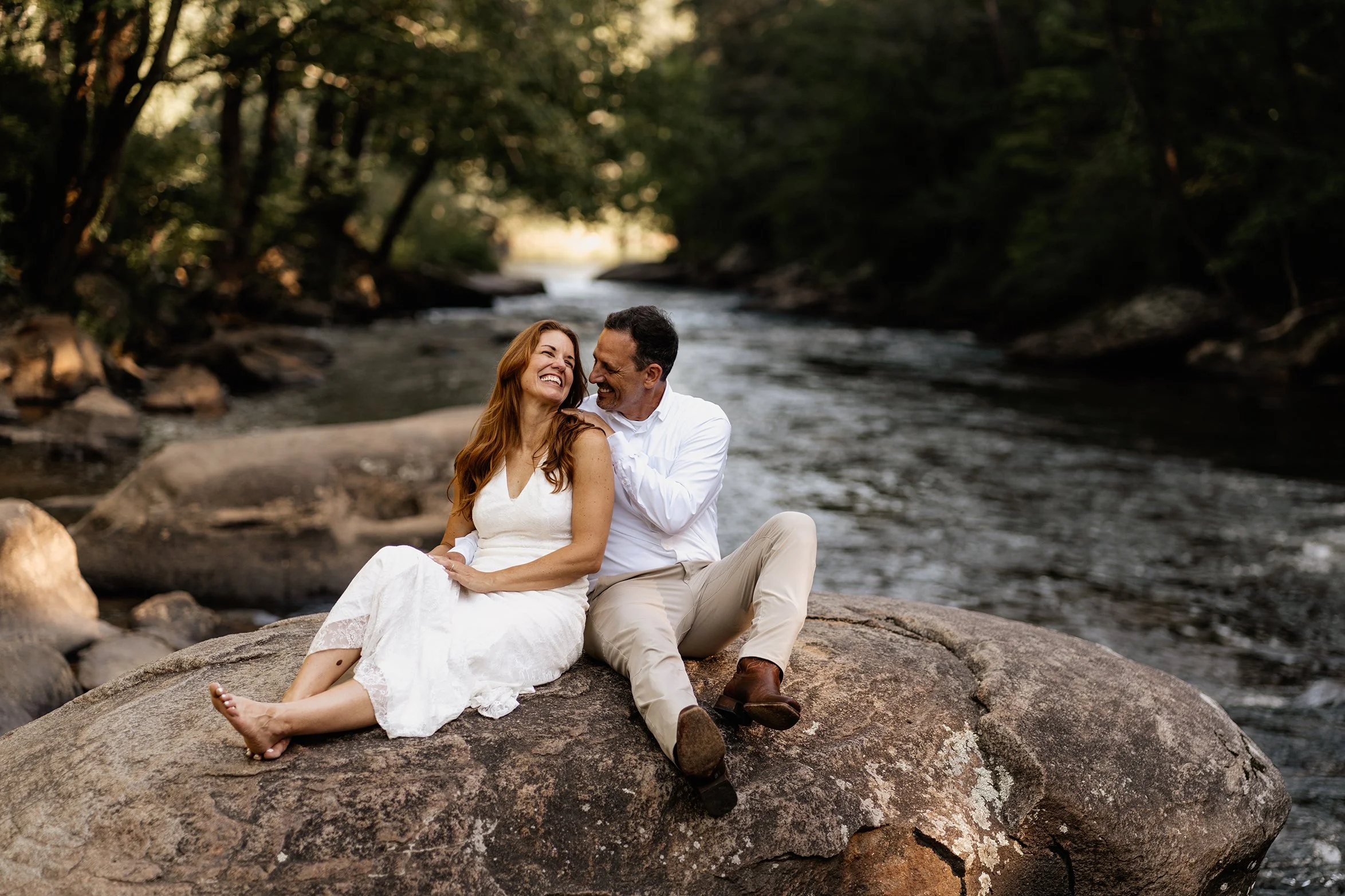 Greg and Stephanie posing together on riverside rocks with fall foliage at their Appalachian wedding