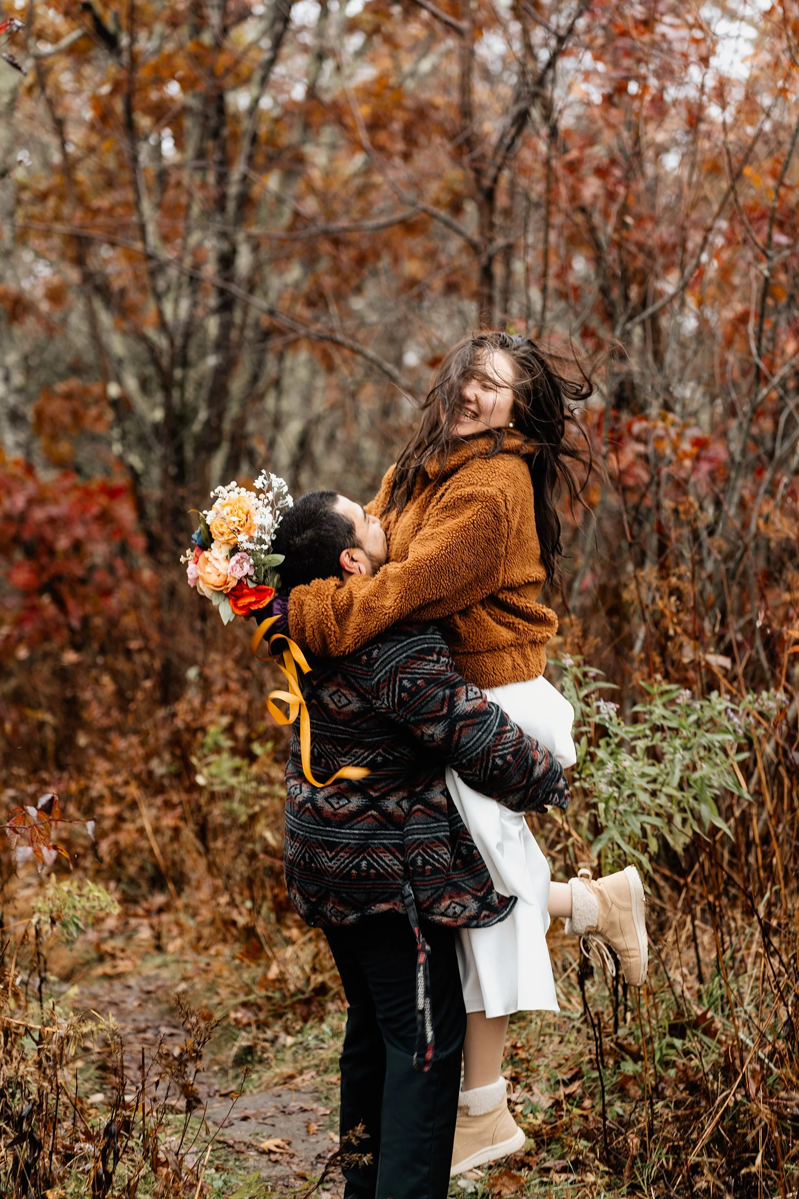 Groom lifting his bride joyfully in an autumn fall forest during their Appalachian elopement