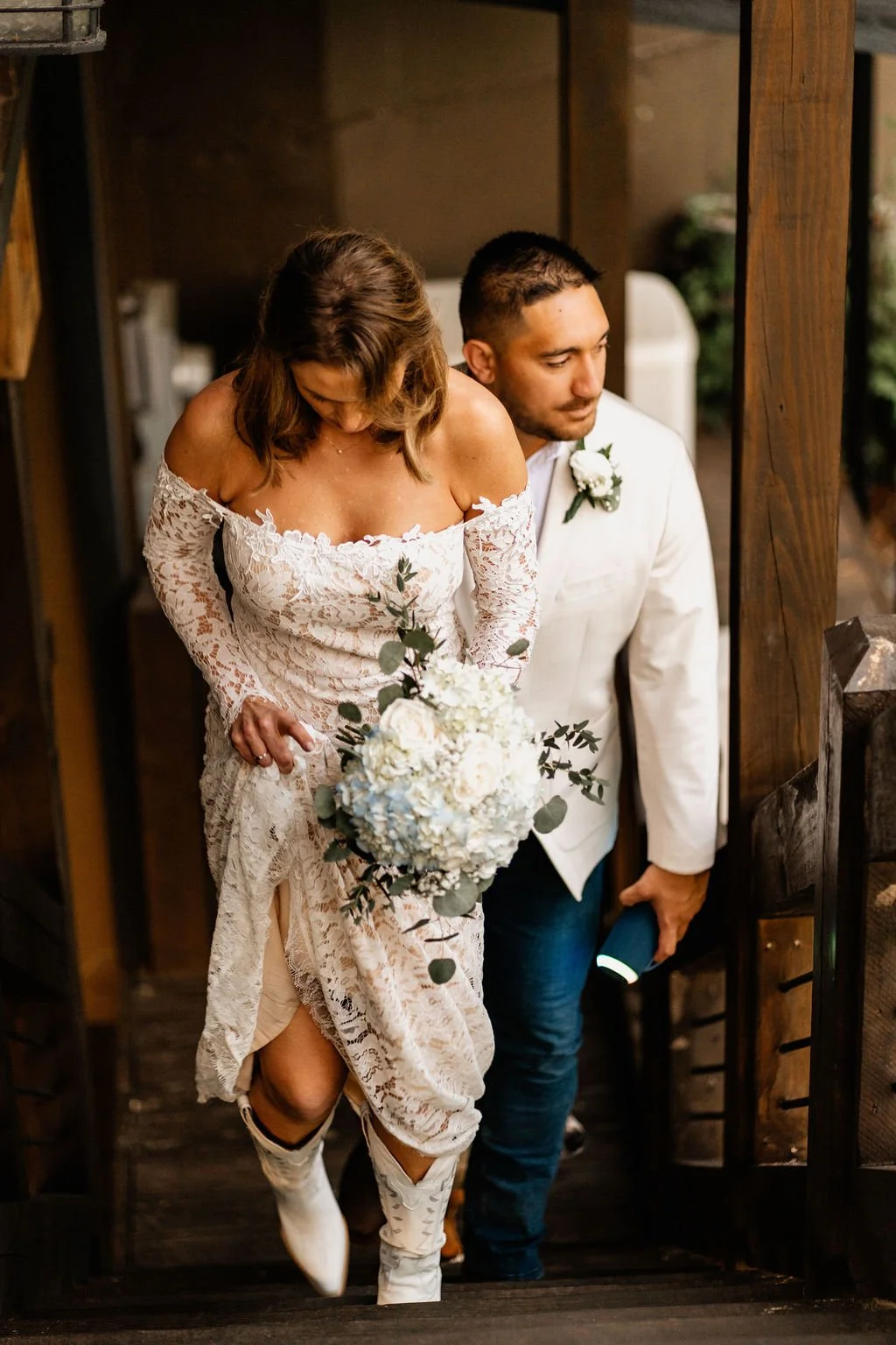 Erin and William stepping out of the cabin doorway together, Erin in her lace gown and white cowboy boots holding her blue hydrangea bouquet, during their Blue Ridge Georgia elopement