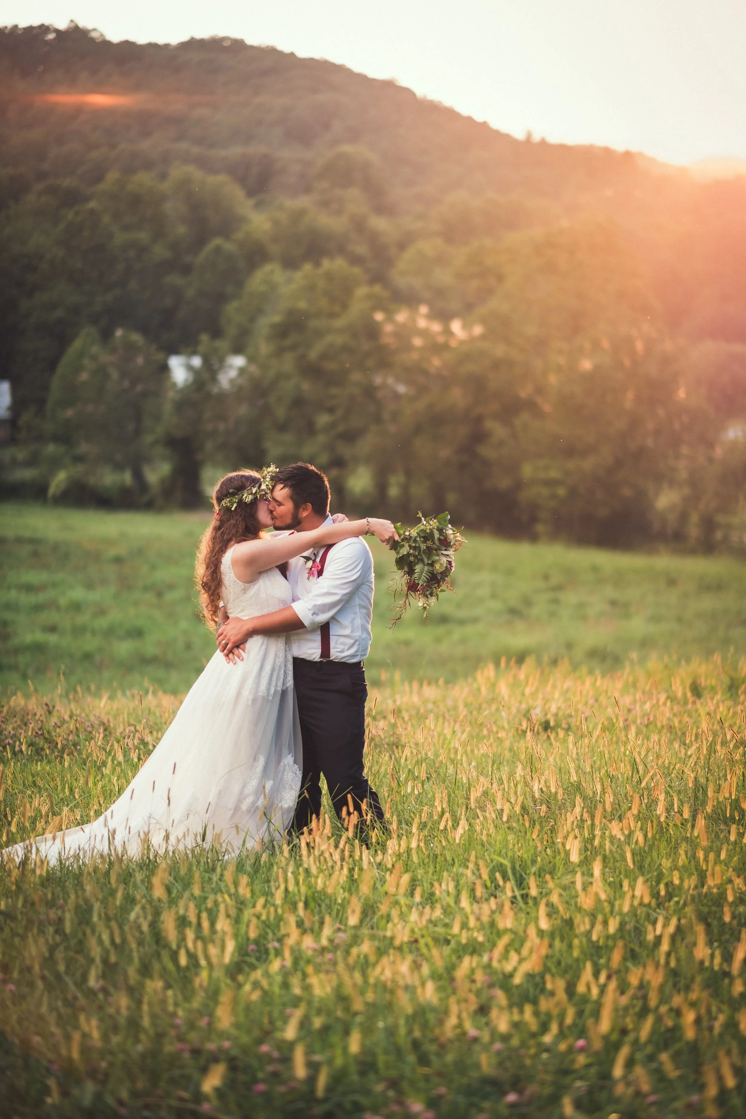 Couple sharing a kiss in a golden meadow at sunset during their Blue Ridge Appalachian mountain wedding