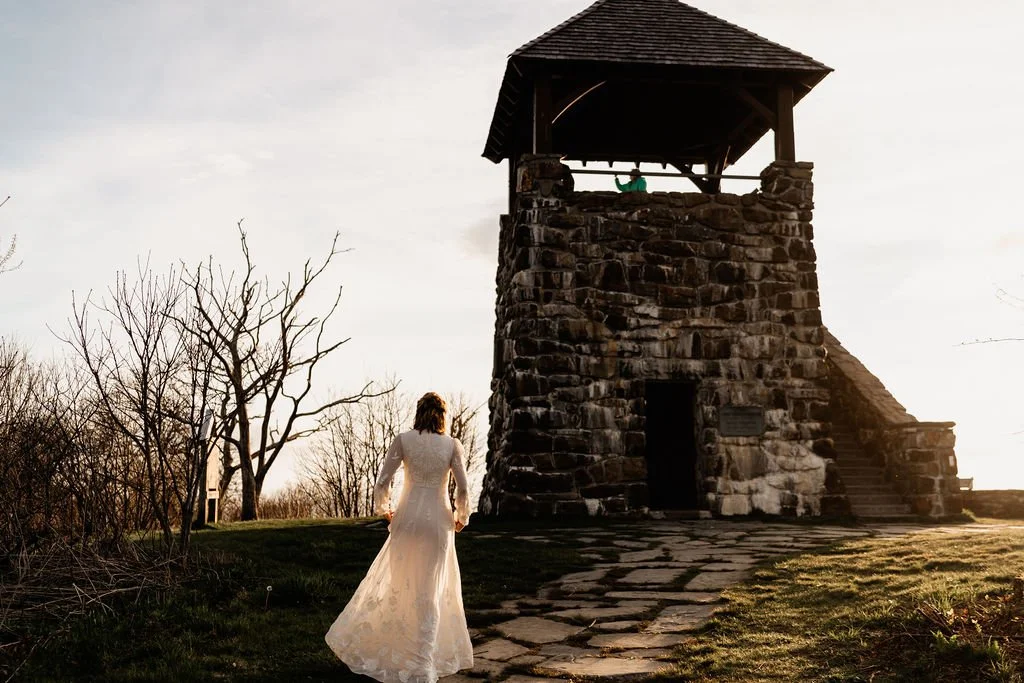 Bride in long lace wedding gown walking toward the Wayah Bald stone fire tower during an intimate mountain elopement in Nantahala National Forest, North Carolina