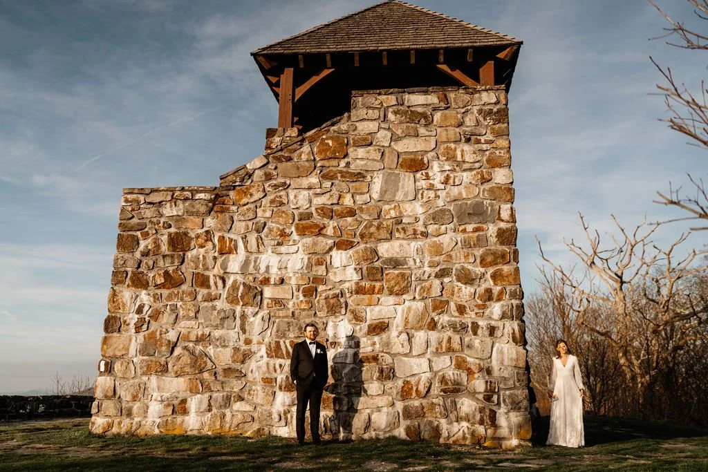 Bride and groom standing together against the stone wall of Wayah Bald fire tower during their intimate Appalachian mountain wedding, Nantahala National Forest NC