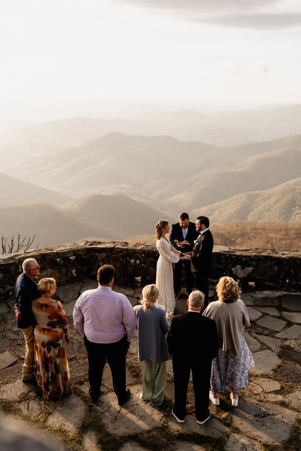 Intimate wedding ceremony on the stone overlook at Wayah Bald summit with sweeping Appalachian mountain panorama, surrounded by close family, Nantahala National Forest NC