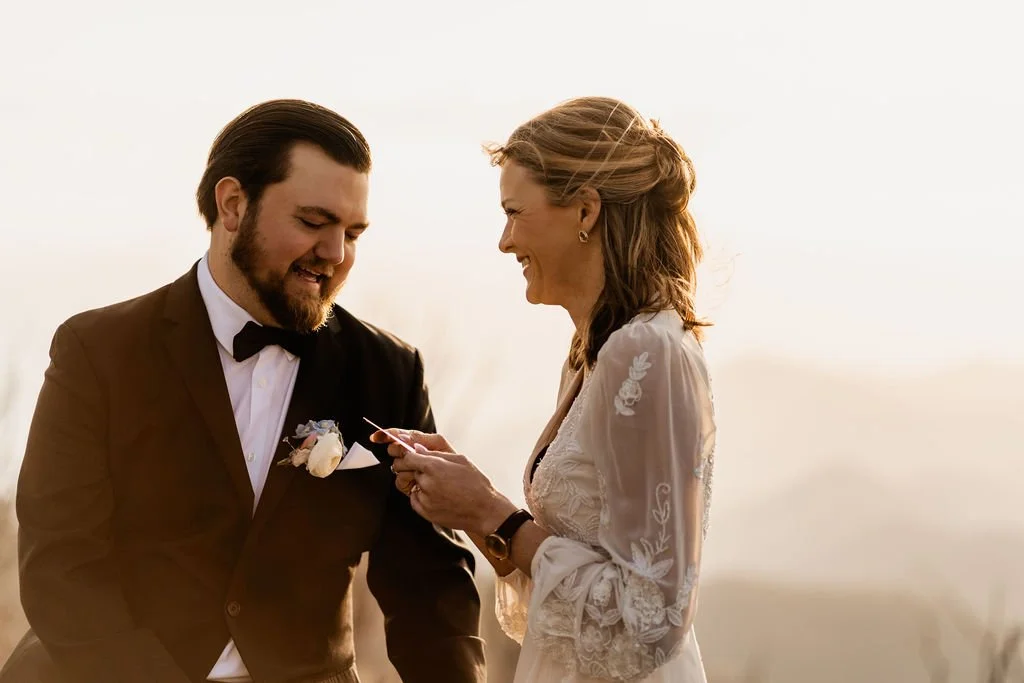 Bride reading handwritten wedding vows from a card while Groom smiles during their intimate mountaintop ceremony at Wayah Bald, Nantahala National Forest NC