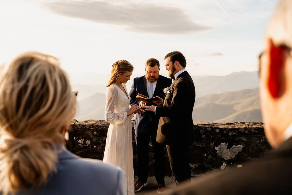 Wide shot of intimate wedding ceremony on the stone overlook at Wayah Bald with family as witnesses and sweeping Appalachian mountain views, Nantahala National Forest North Carolina