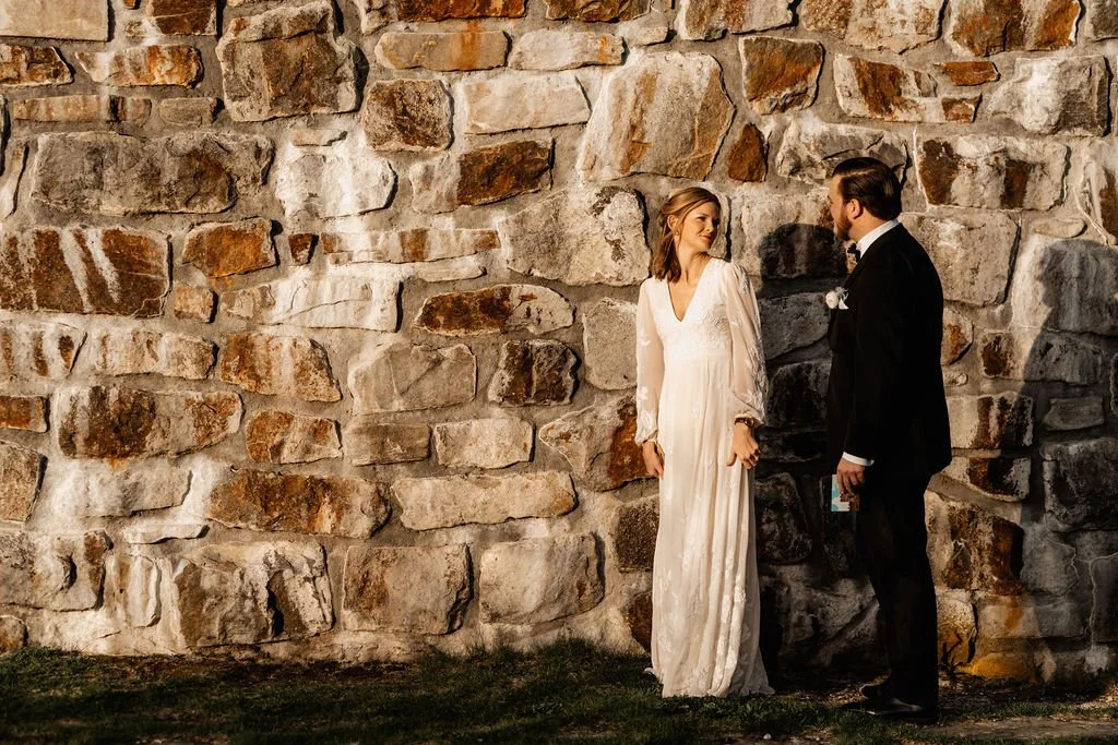 Bride and groom standing close together against the historic stone wall of Wayah Bald fire tower, gazing at each other during their intimate Appalachian mountain wedding