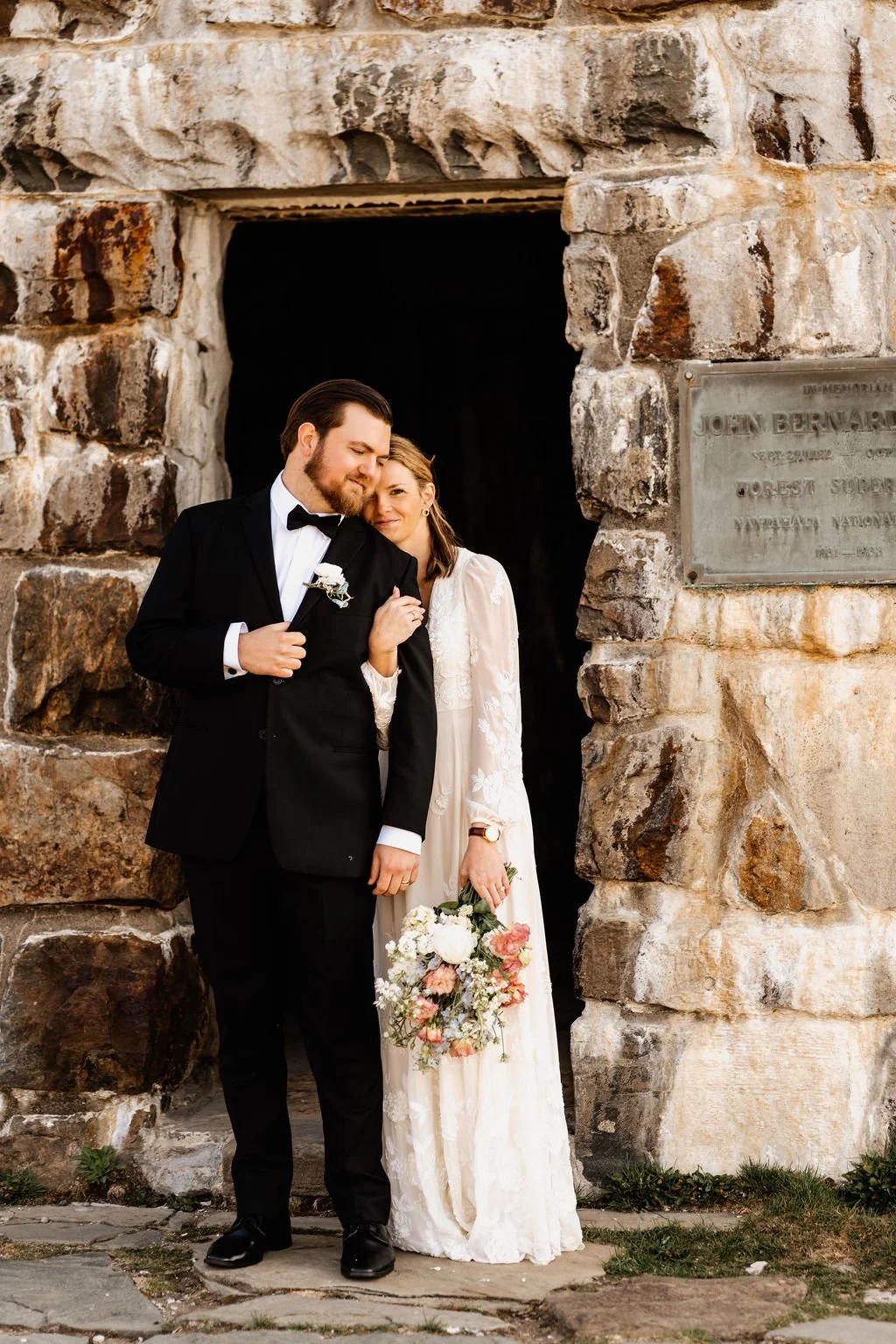Bride resting her head on groom's shoulder against the Wayah Bald tower dedication plaque during their intimate Appalachian mountain elopement, Nantahala National Forest North Carolina