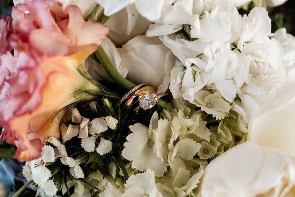 Close-up of bridal bouquet with white roses, blush flowers, and greenery with diamond engagement ring nestled among the blooms at Wayah Bald mountain wedding, NC