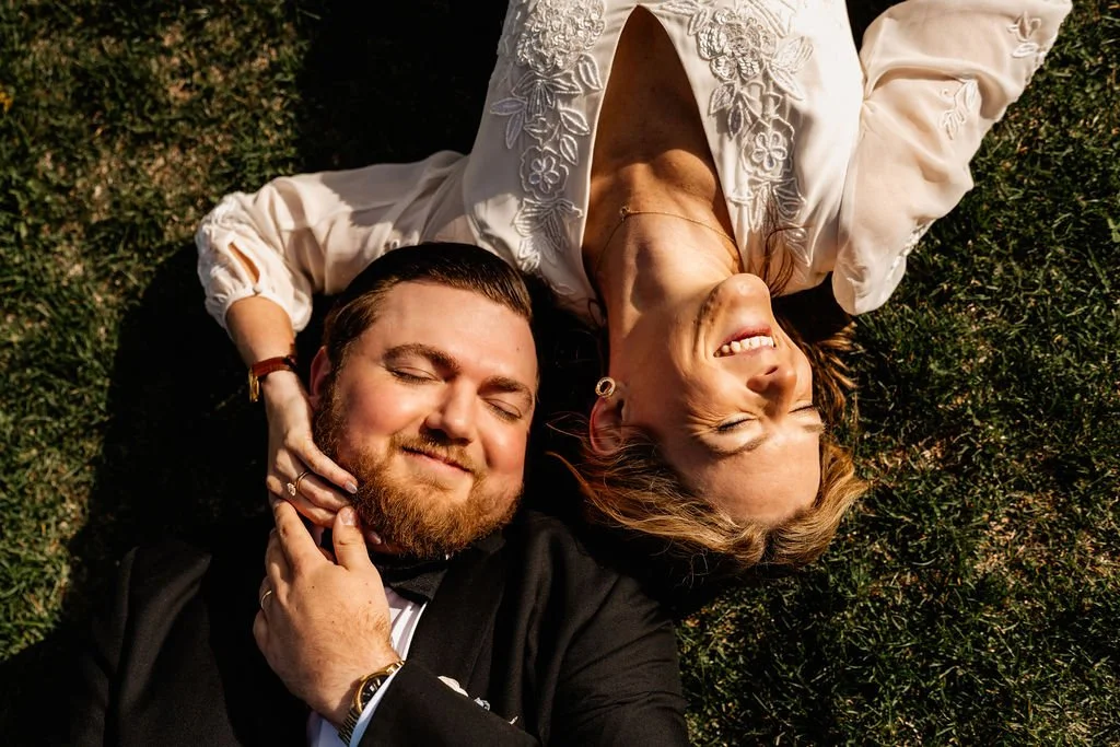 Bride and groom laughing joyfully while lying in the grass at Wayah Bald summit after their intimate mountain elopement ceremony, Nantahala National Forest North Carolina