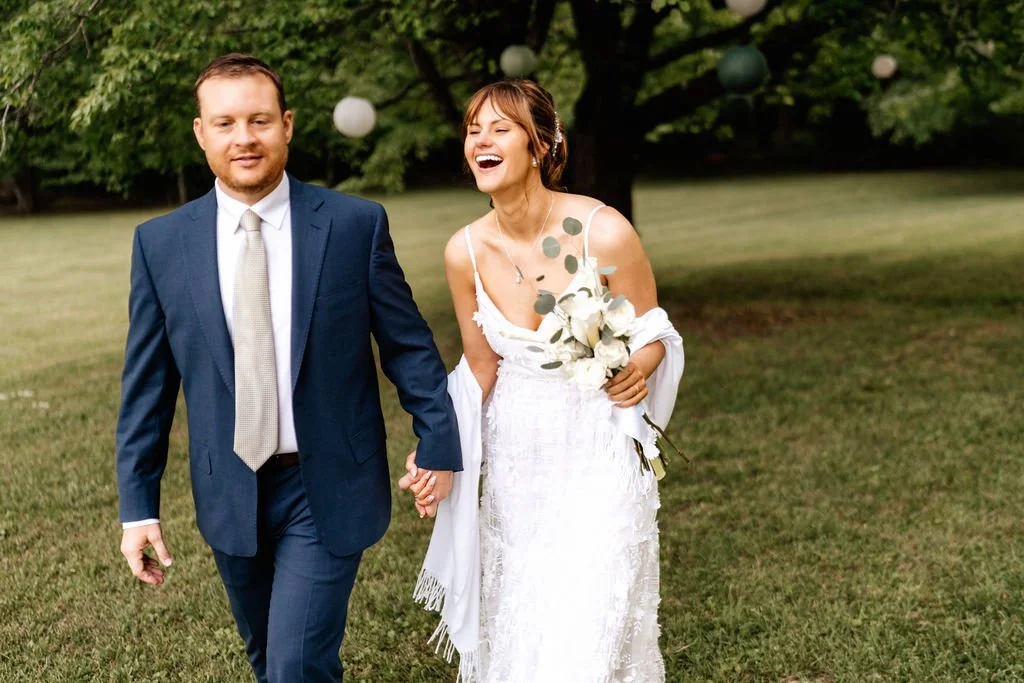 Laughing bride and groom walking together on a green lawn with paper lanterns in the background at a joyful Blue Ridge, Georgia wedding