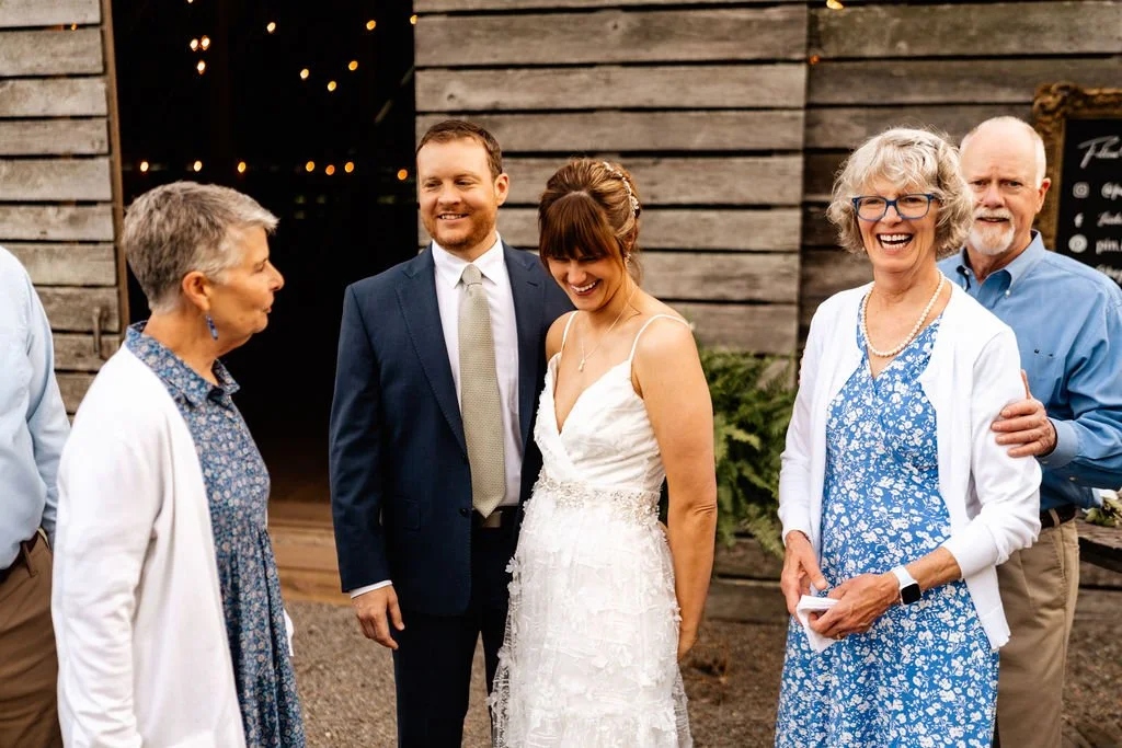 Bride and groom greeting smiling family members outside a lit rustic barn after their wedding ceremony in Blue Ridge, Georgia