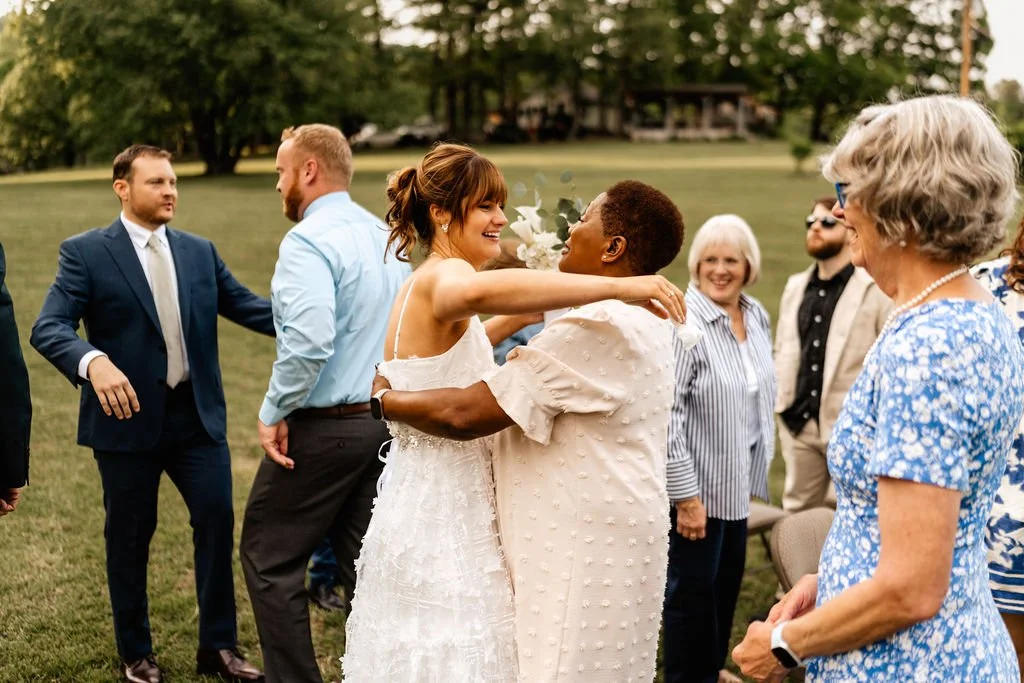Bride embracing a smiling guest surrounded by family and friends on the lawn after an outdoor wedding ceremony in Blue Ridge, Georgia