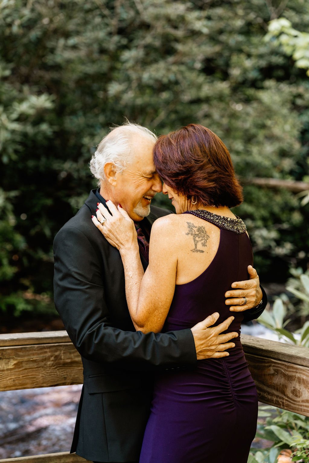 Older couple embracing forehead to forehead on a wooden bridge at their dawn elopement at Helton Creek Falls in Blue Ridge, Georgia