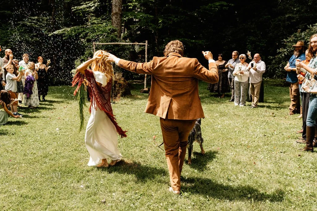 Hope and Chase during their wedding recessional with guests cheering around them in the forest clearing at Huffman Creek, Robbinsville, North Carolina