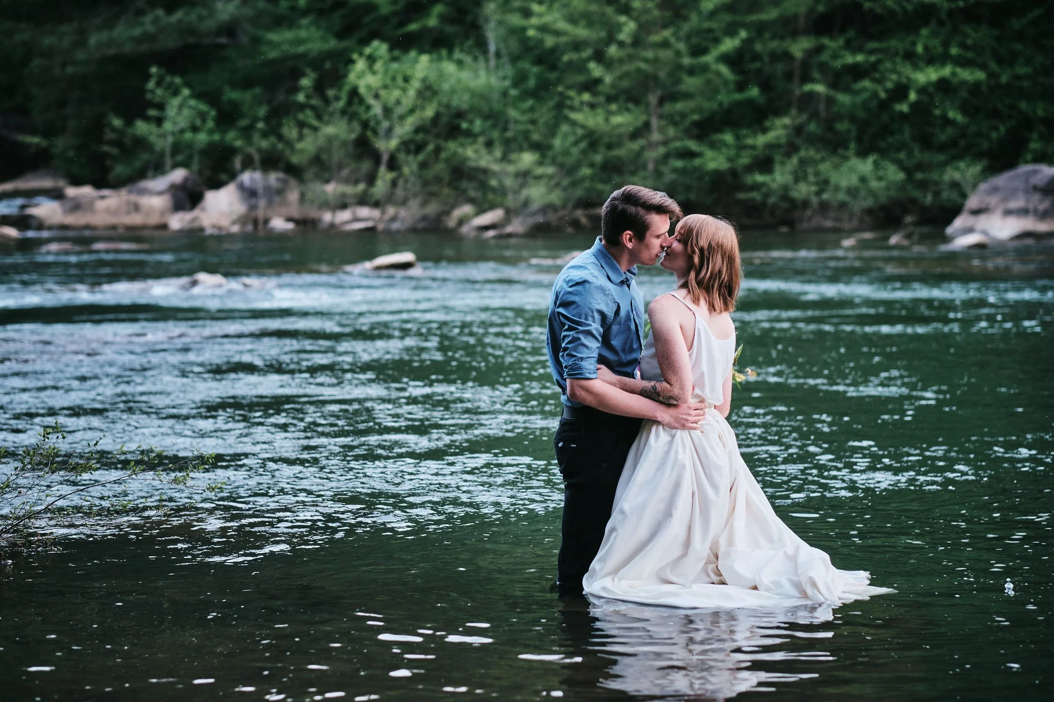 Margo holding a lush wildflower bouquet while leaning into Keene along a North Georgia riverbank during their Blue Ridge Georgia elopement, Appalachian Wedding Photography