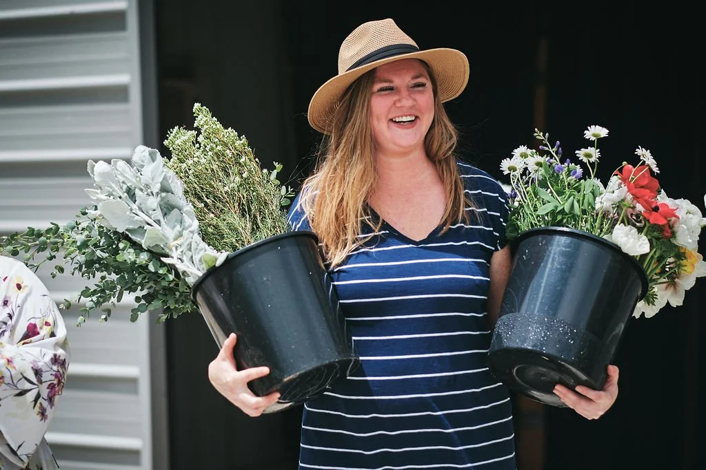 Woman in a straw hat carrying two black buckets overflowing with fresh wildflowers for a Blue Ridge Georgia elopement