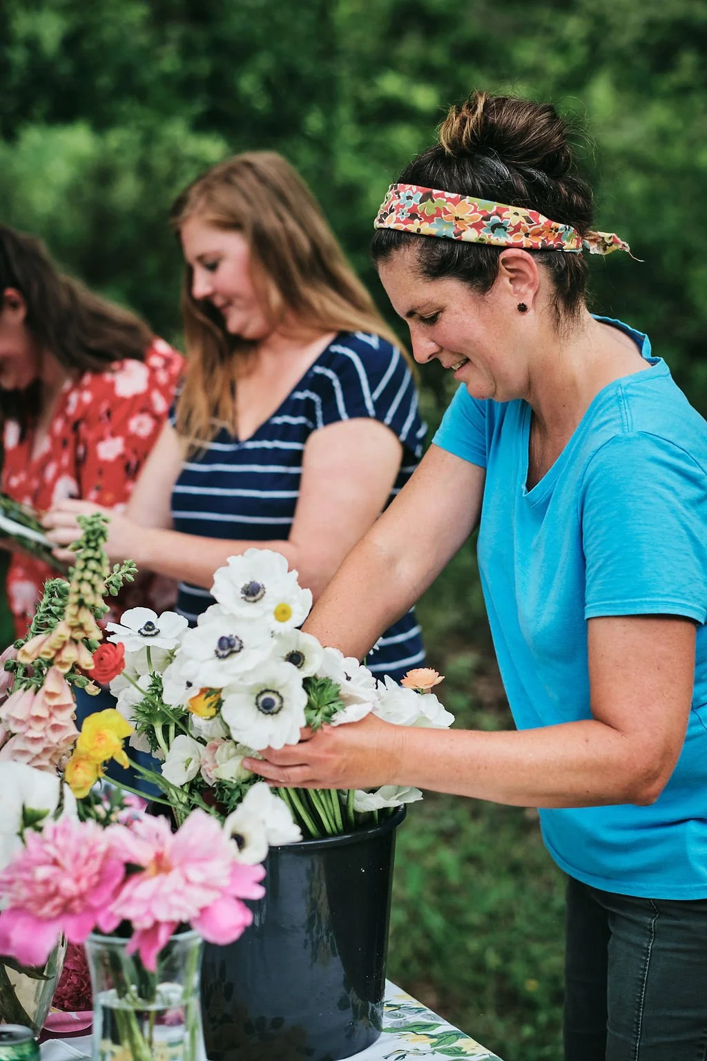 Woman holding a white anemone flower arrangement at an outdoor table with another woman arranging blooms behind her in Blue Ridge Georgia